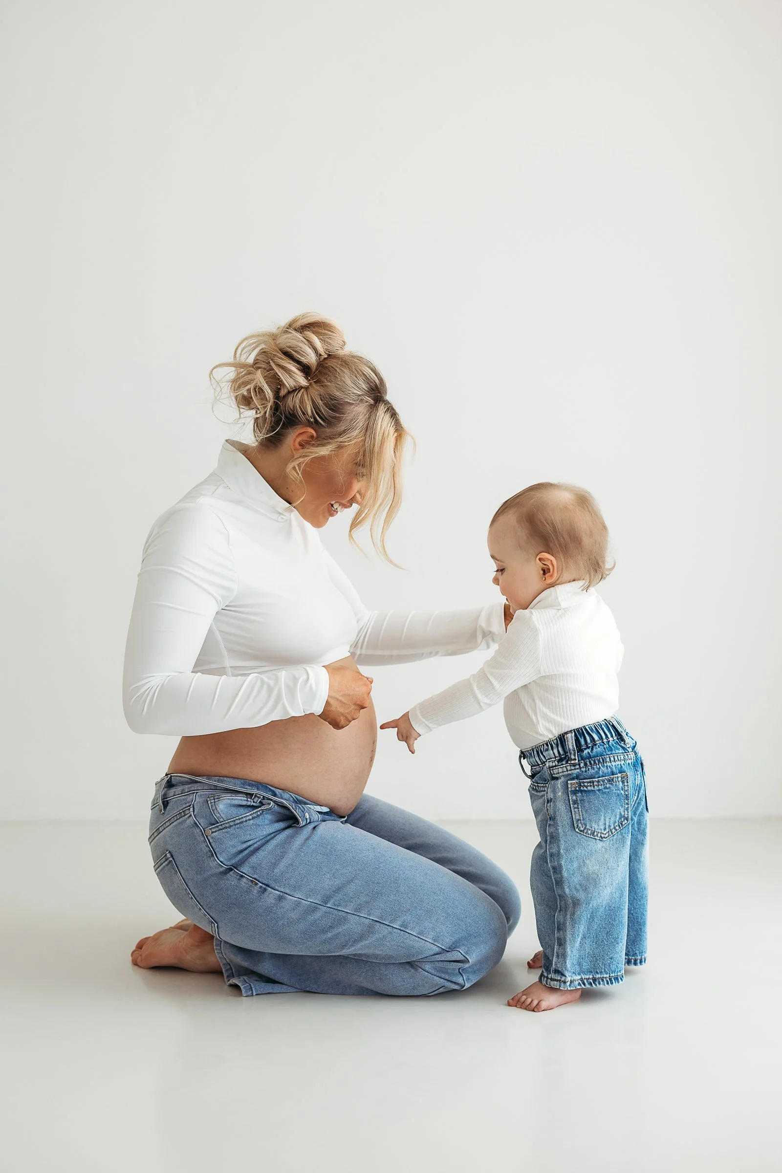 Pregnant mum smiling with her young daughter as she points to her baby bump during a studio maternity session.