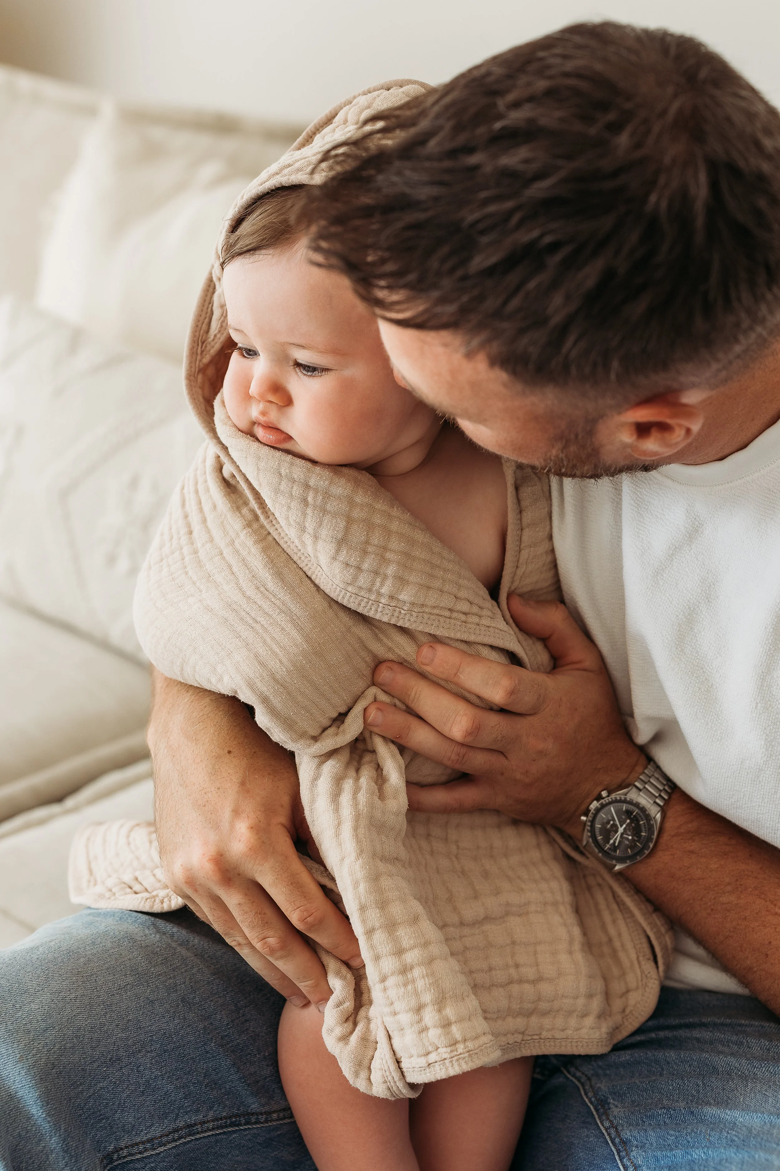 Father cuddling his young child and kissing their cheek during a relaxed first birthday photography session