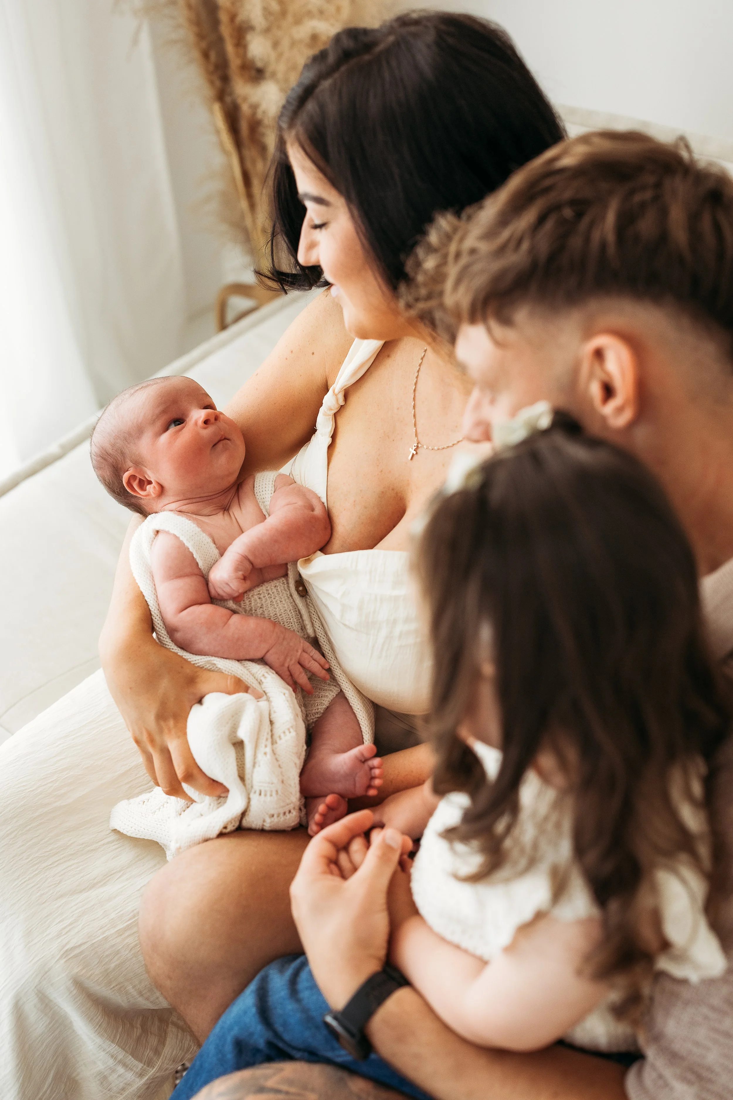 Mum cuddling her newborn baby with older sibling and dad during a relaxed family newborn session.