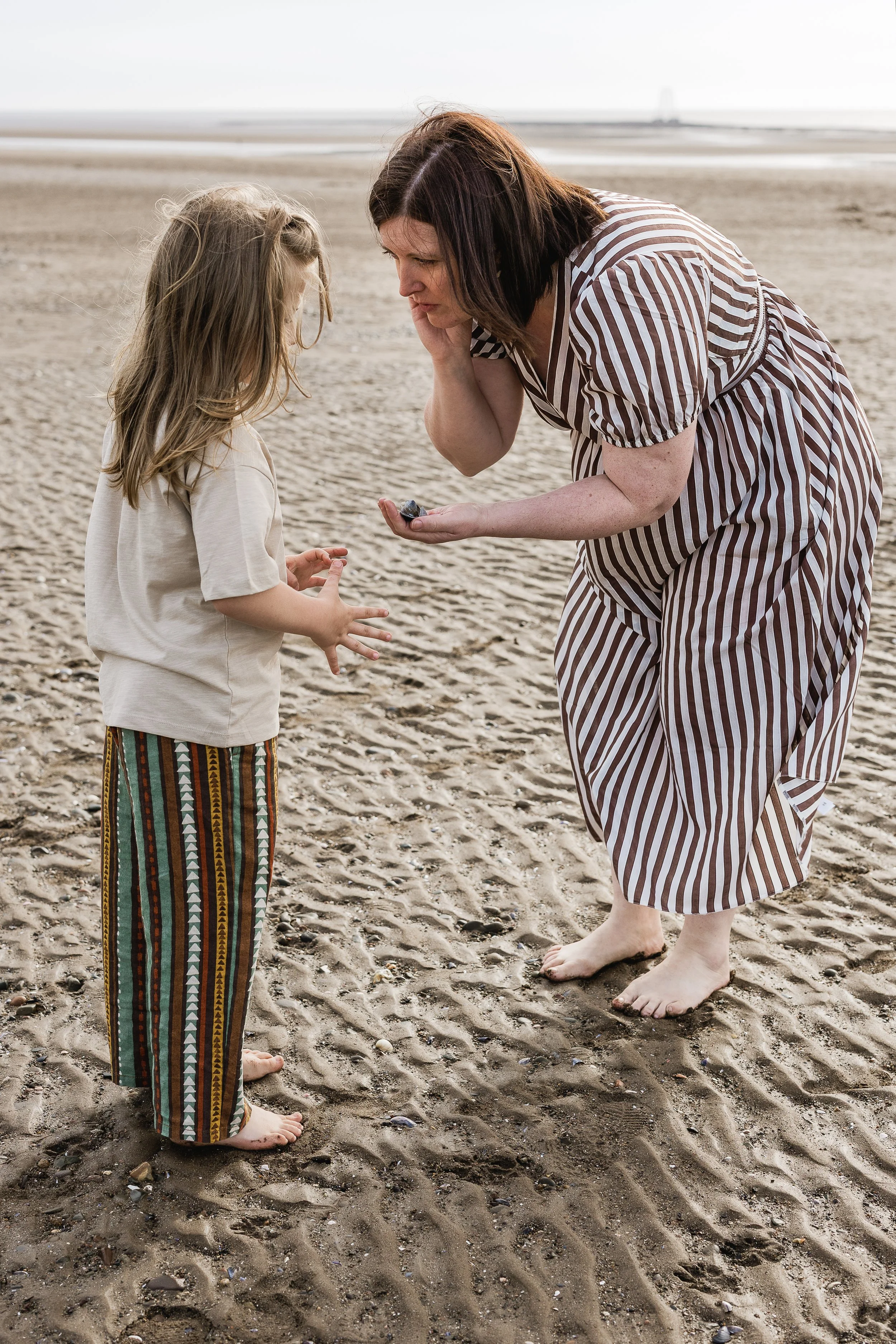 A mother and son sharing a playful moment together by the sea, capturing their connection and the joy of childhood.