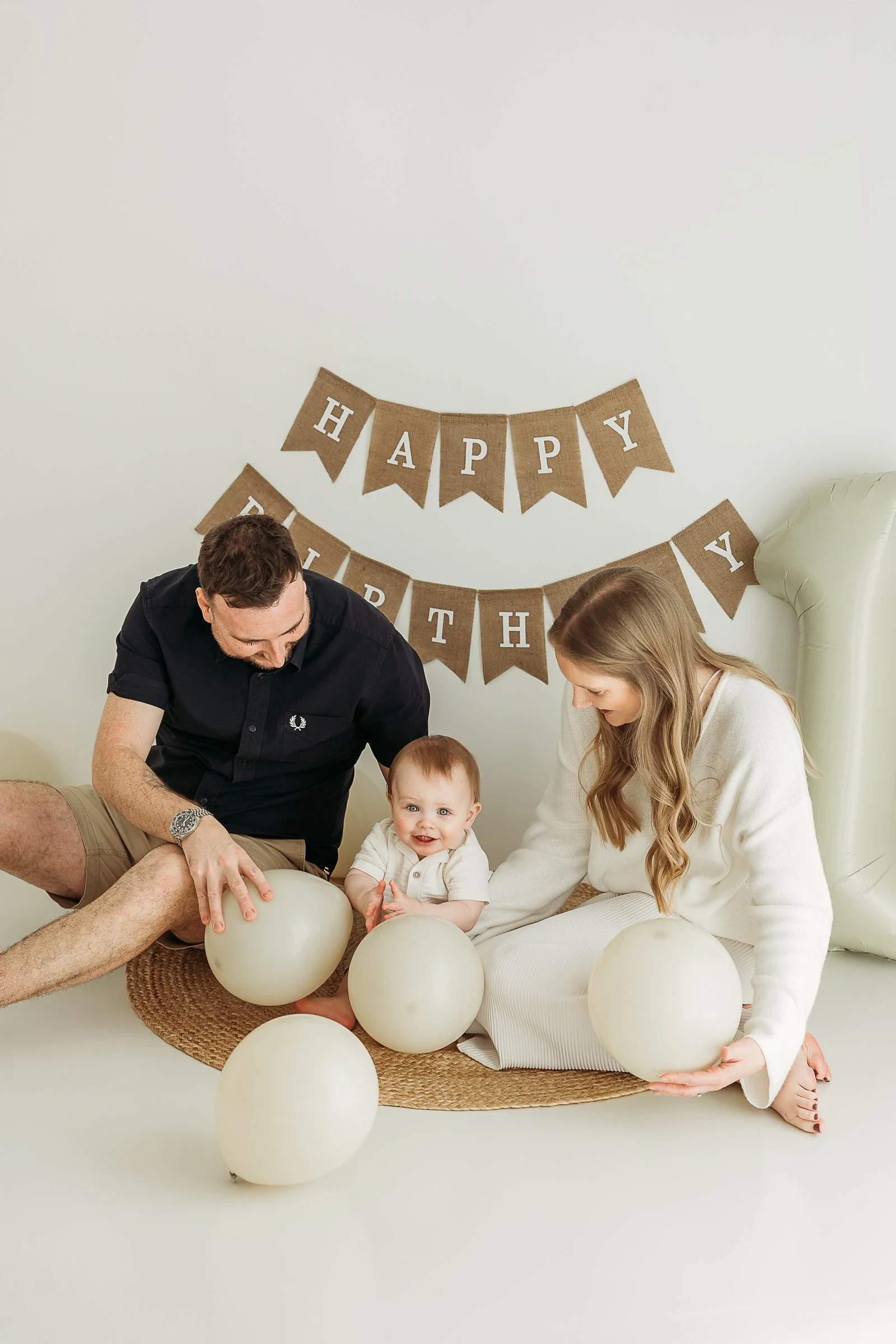 Family celebrating a child’s first birthday together with balloons and birthday decorations in a natural light studio