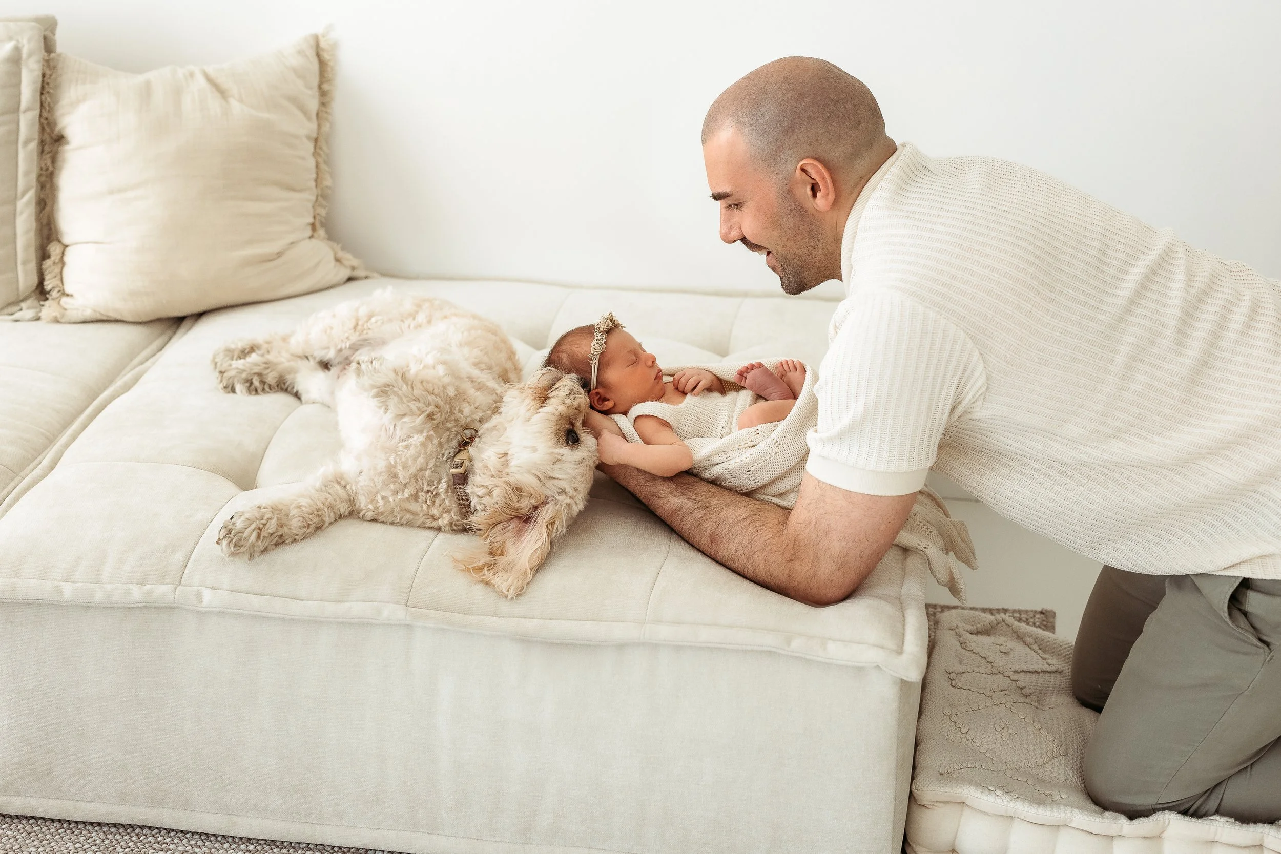 Father sharing a gentle moment with his newborn baby and family dog during a relaxed newborn photography session.