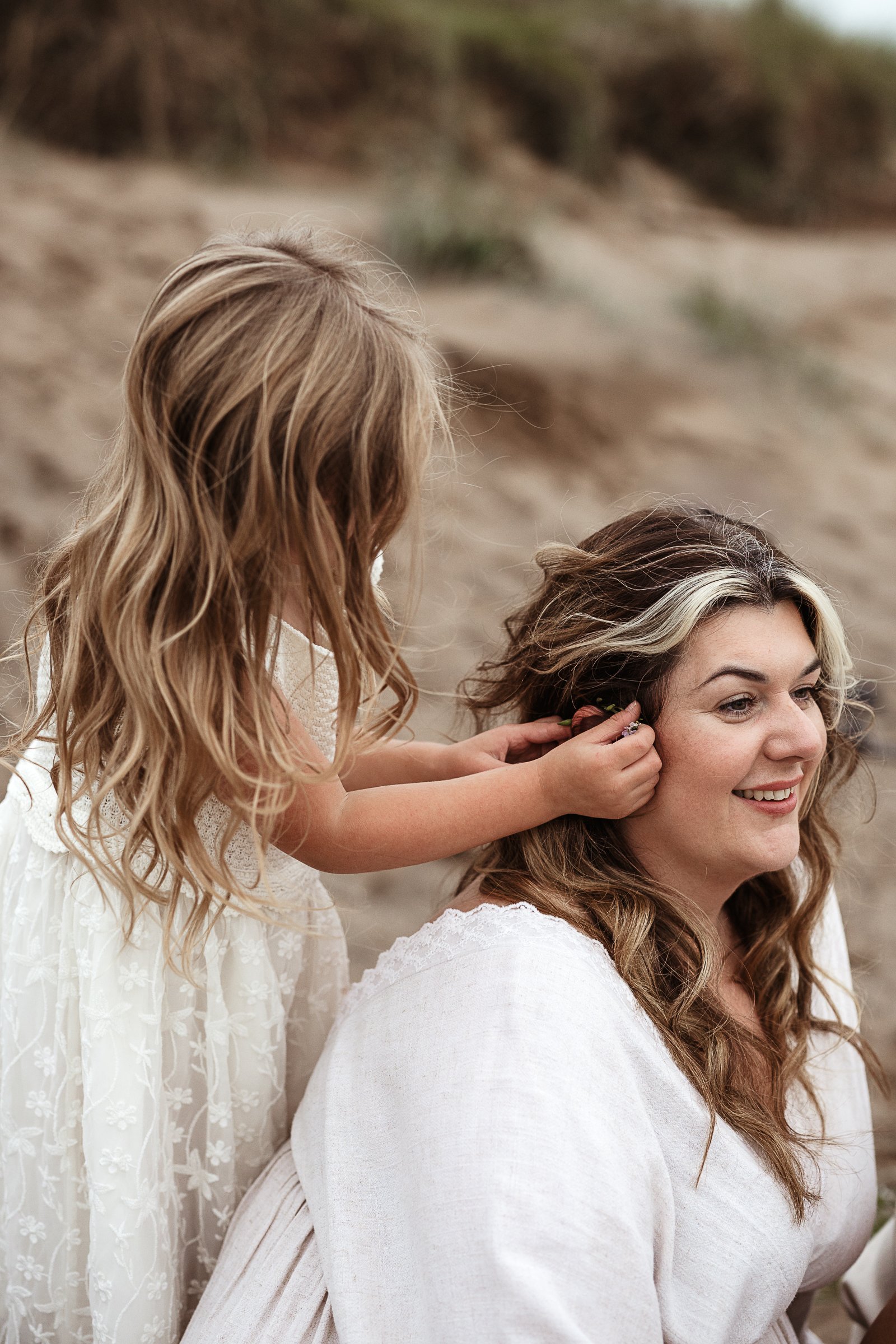 A quiet moment of connection and laughter between two a daughter and mother during a beach family session.