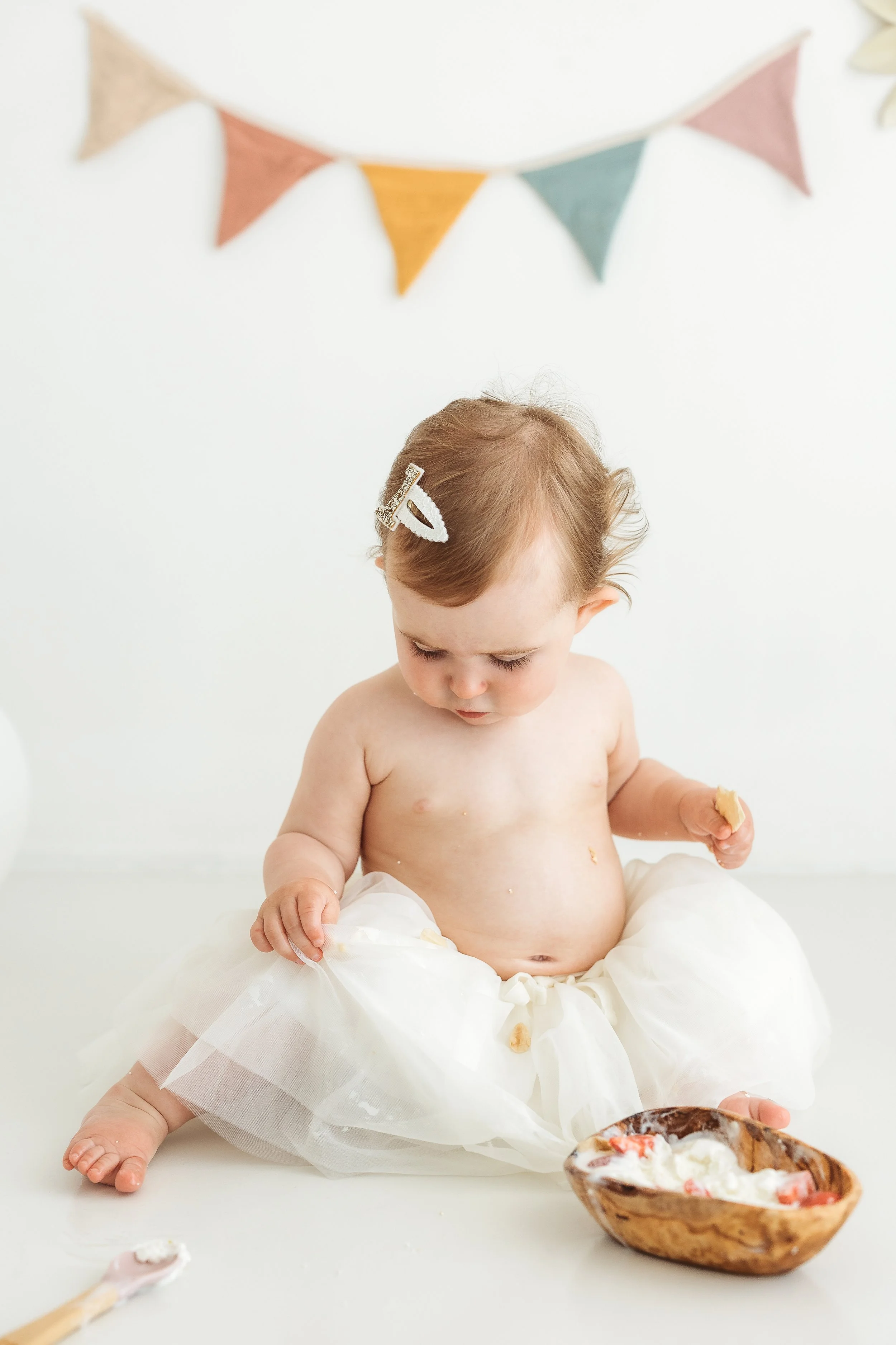 One year old child enjoying ice cream during a first birthday photography session with colourful birthday decorations