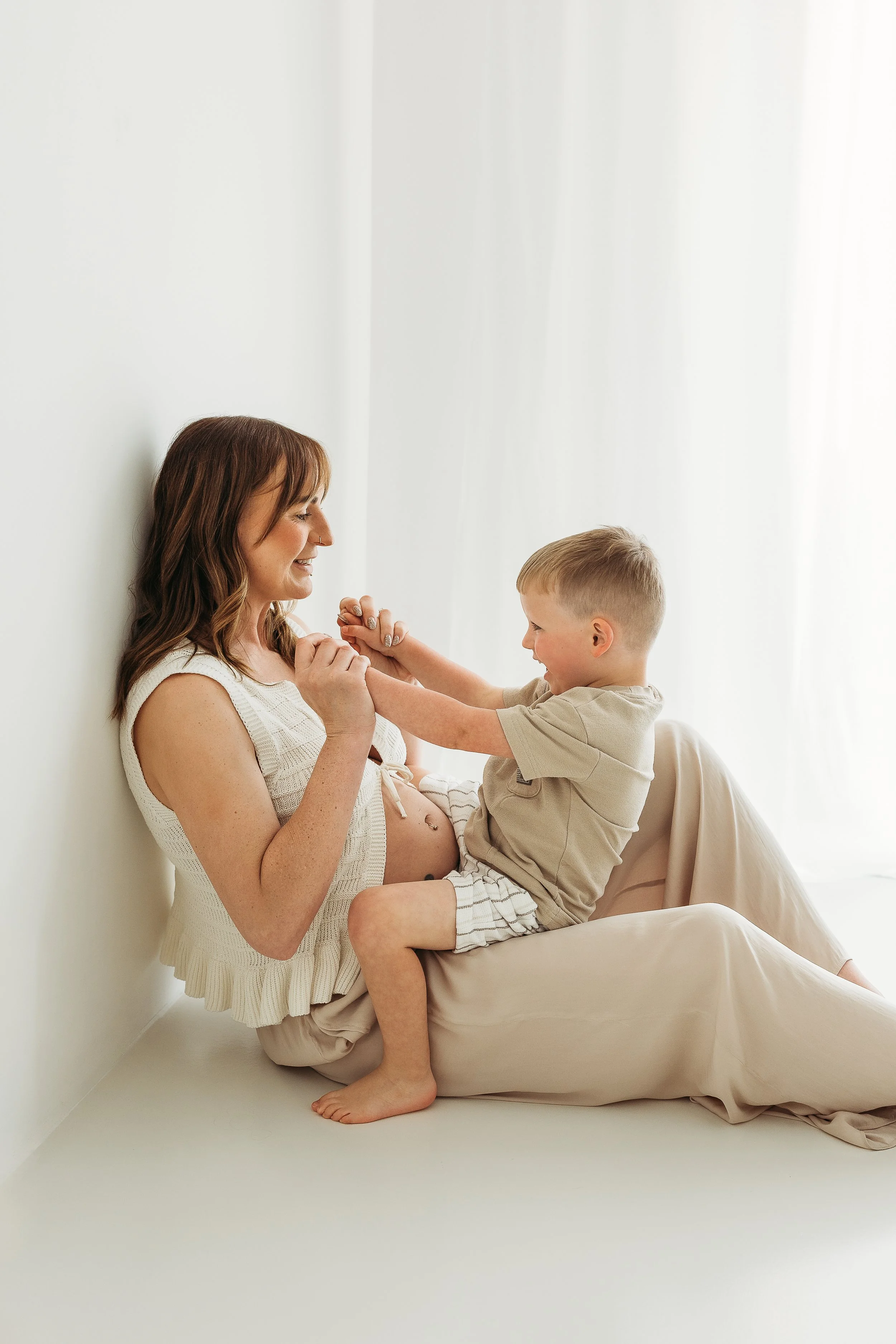 A mother and young son sharing a loving moment together during a maternity photography session, celebrating the arrival of a new baby.