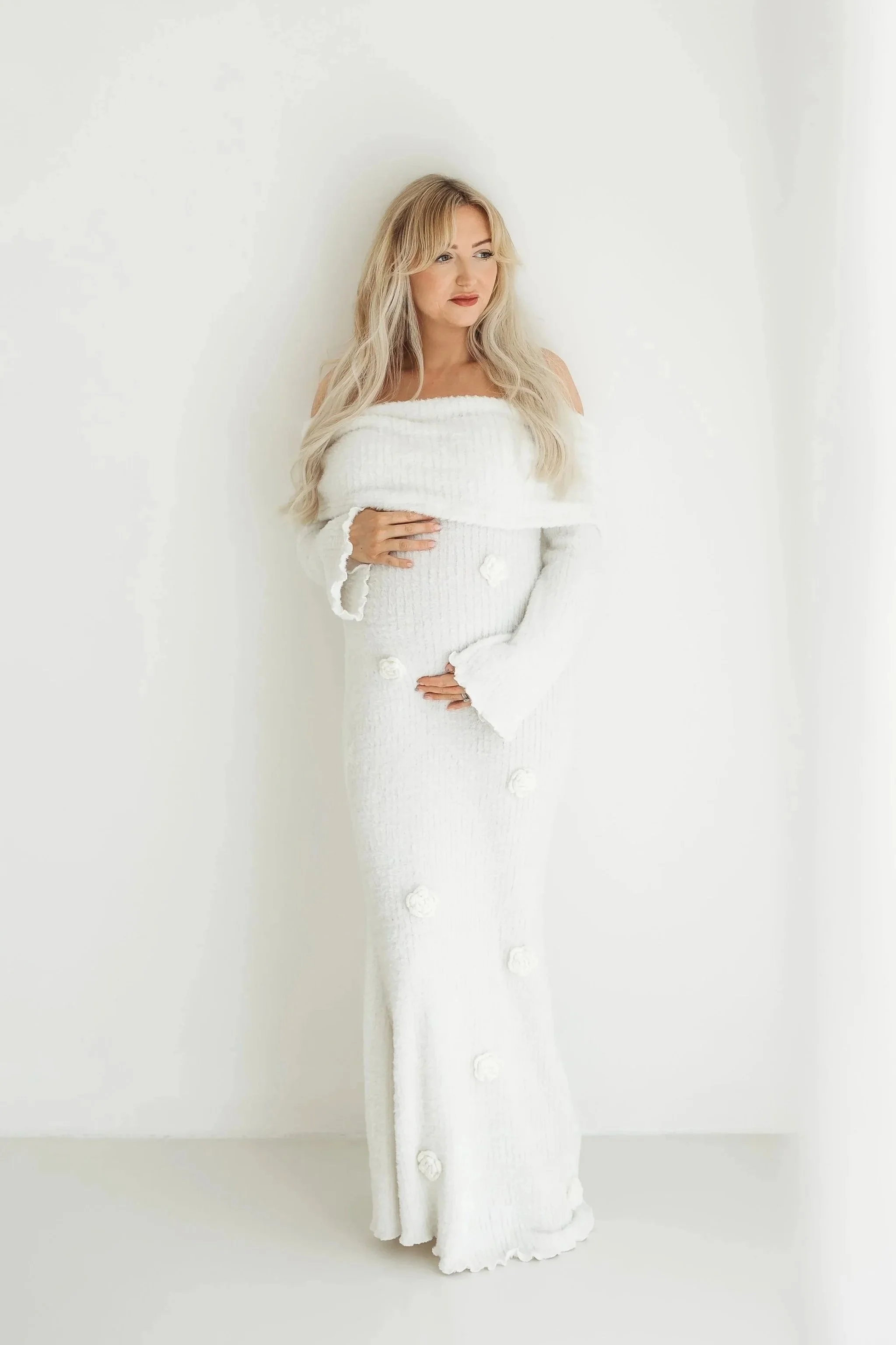 Pregnant woman wearing a white dress during a relaxed studio maternity session.