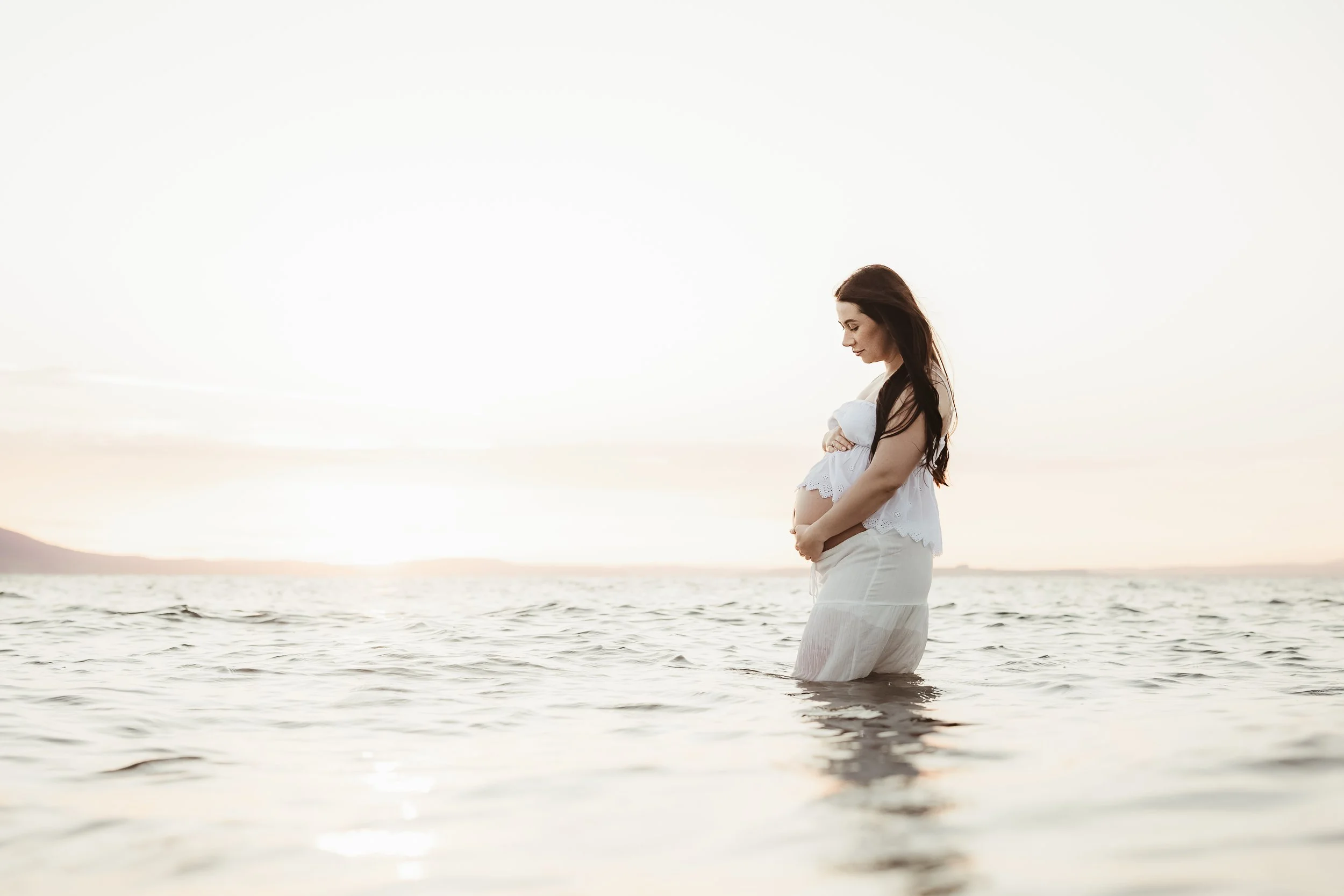 Expectant mother embracing her pregnancy during a beautiful outdoor maternity photography session by the sea.