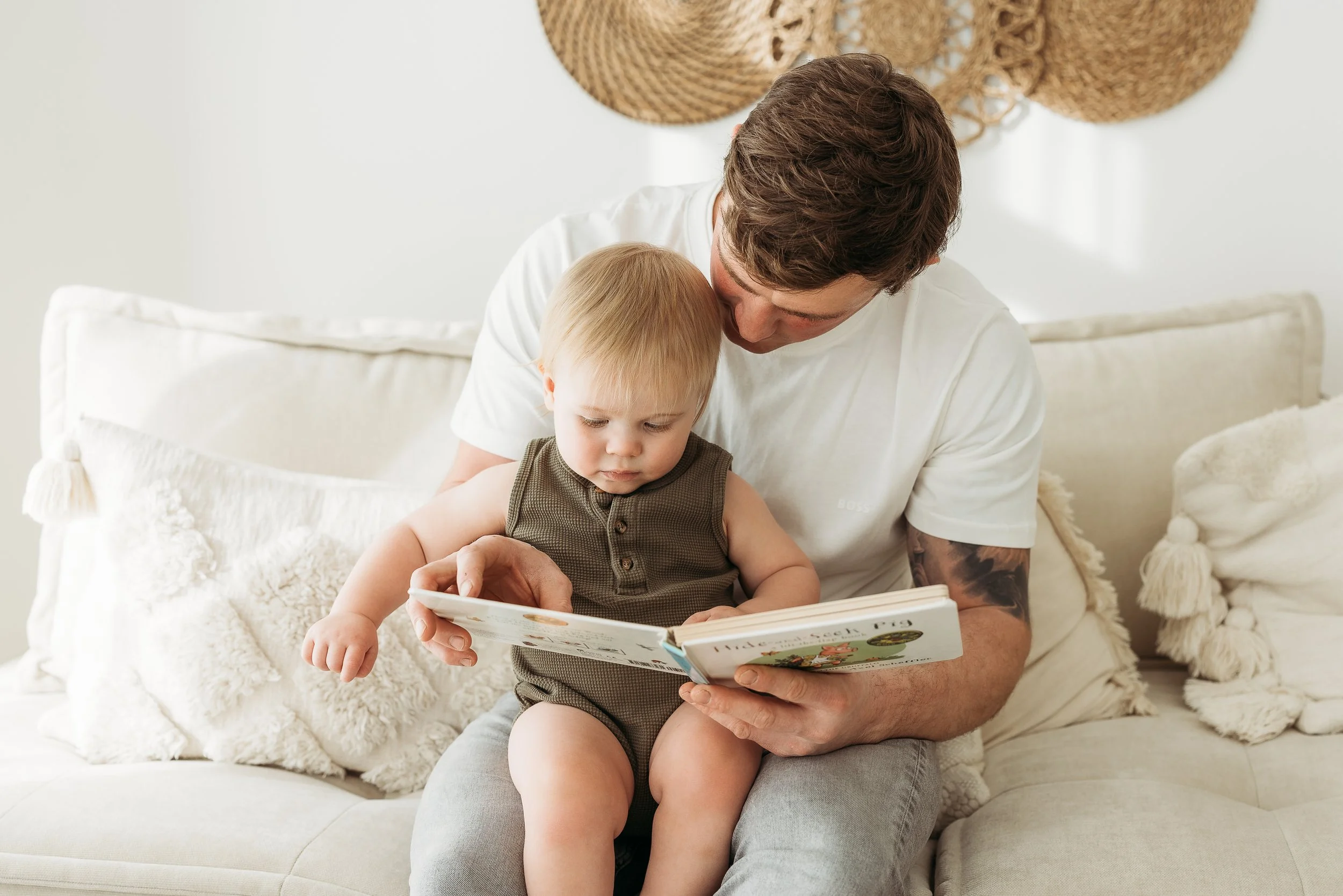 Father sharing a quiet story moment with his young son on a sofa during a relaxed first birthday photography session