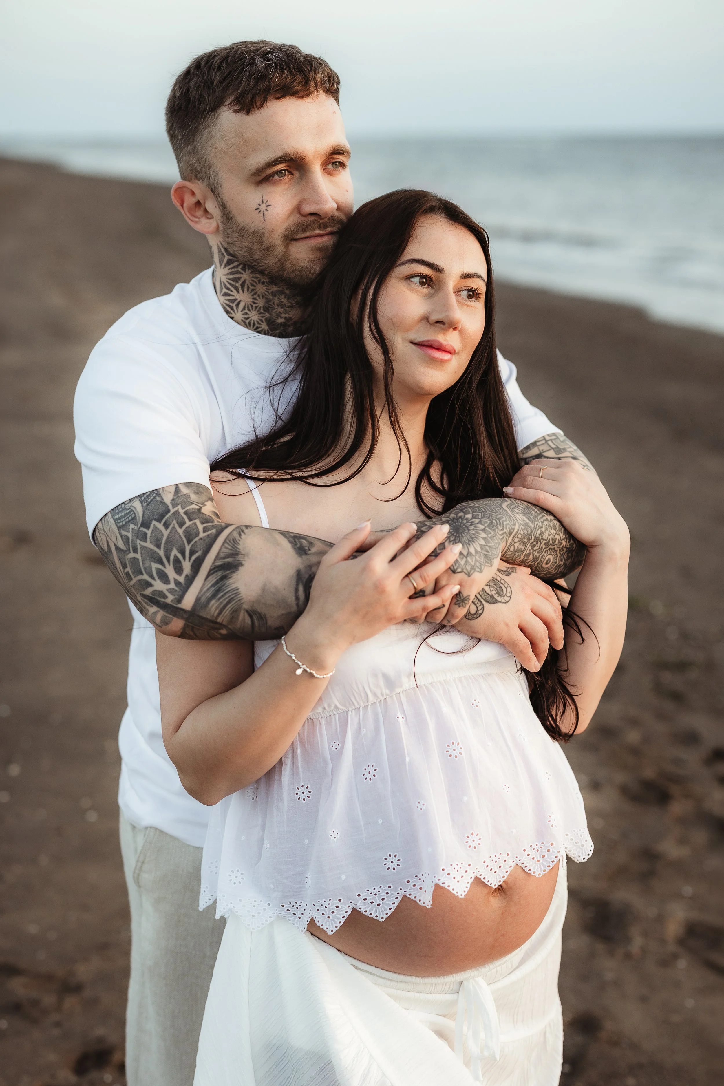 Expectant couple embracing on the beach during a relaxed outdoor maternity photography session.