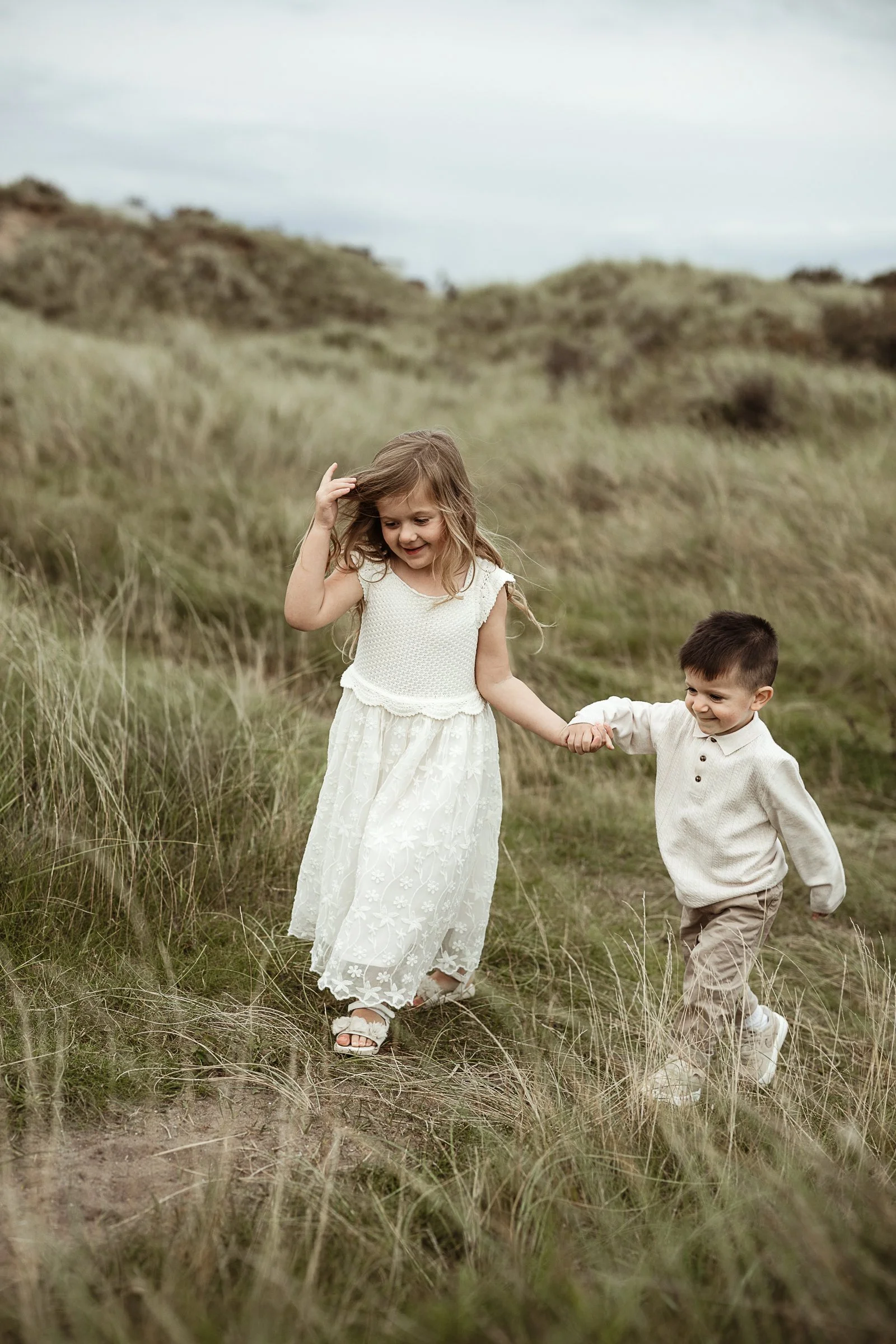 Two siblings walking hand in hand through a grassy field, capturing their bond, curiosity and the simple joy of childhood.
