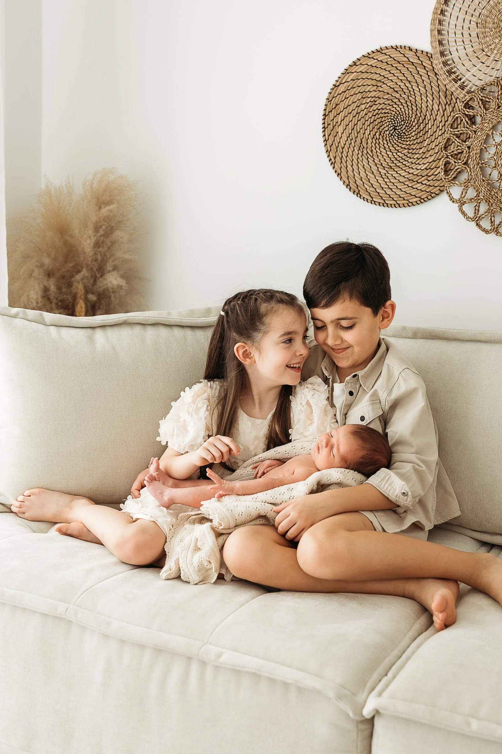 Siblings cuddling their newborn baby during a relaxed newborn family photography session.