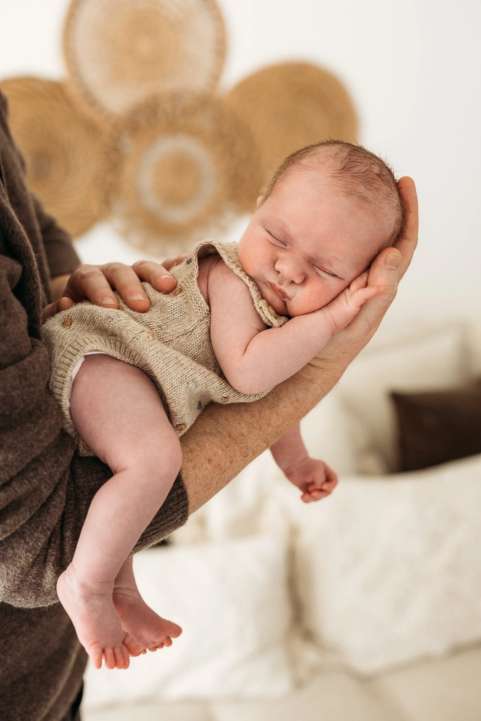 Tiny newborn baby being gently held during a natural newborn photography session.