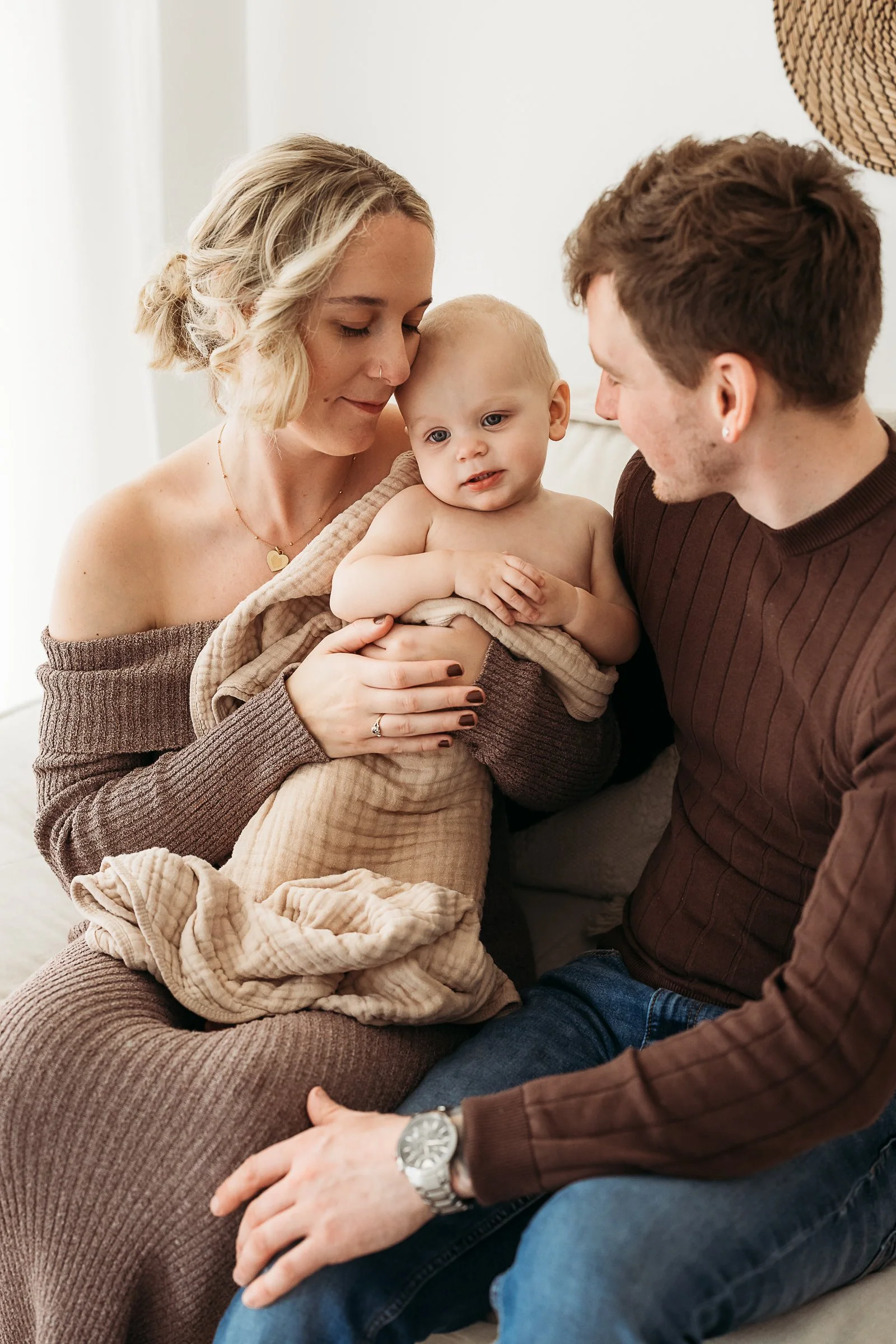 Parents cuddling their newborn baby together in a warm, intimate home-style setting.