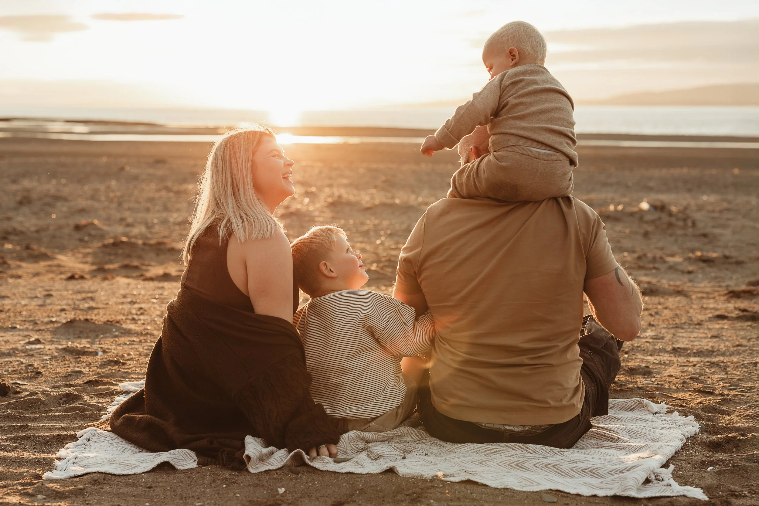 A family enjoying a peaceful moment together by the beach at sunset, capturing love, connection and the magic of slowing down together.