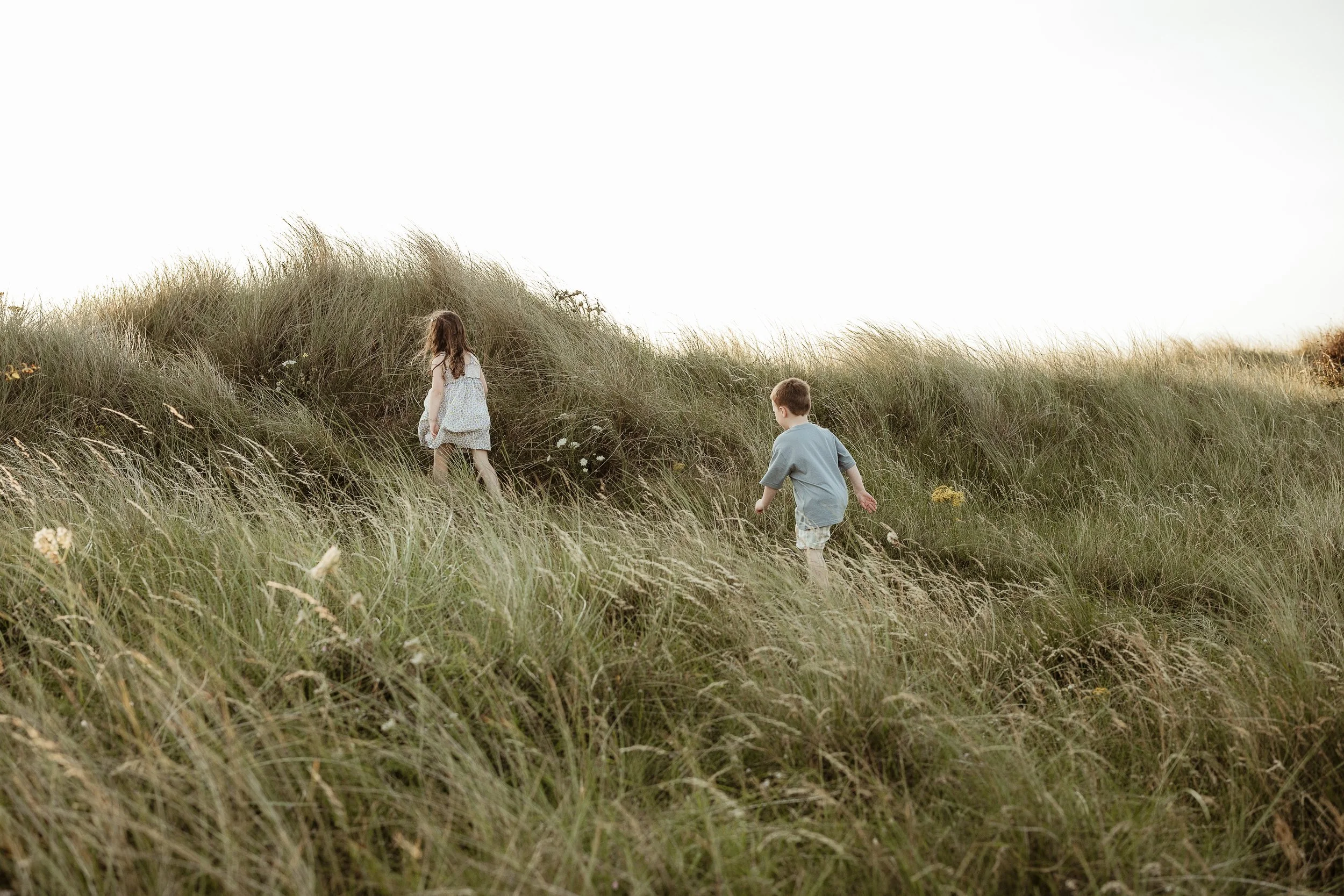 Children walking together through the dunes during a relaxed family photography session.
