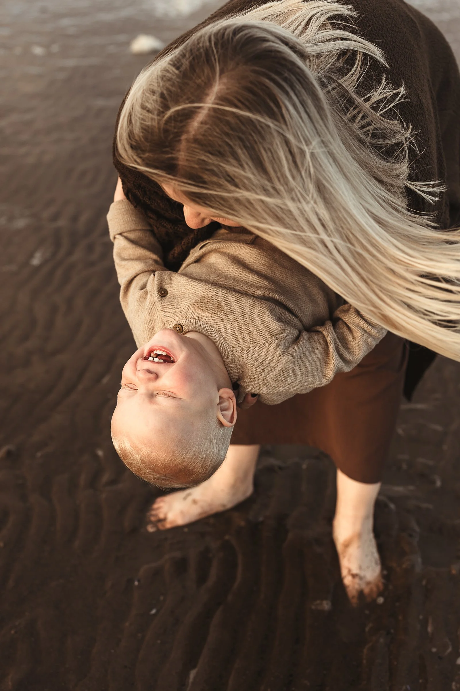 A mother and child sharing a playful beach moment, capturing the laughter, connection and joy found in everyday adventures.