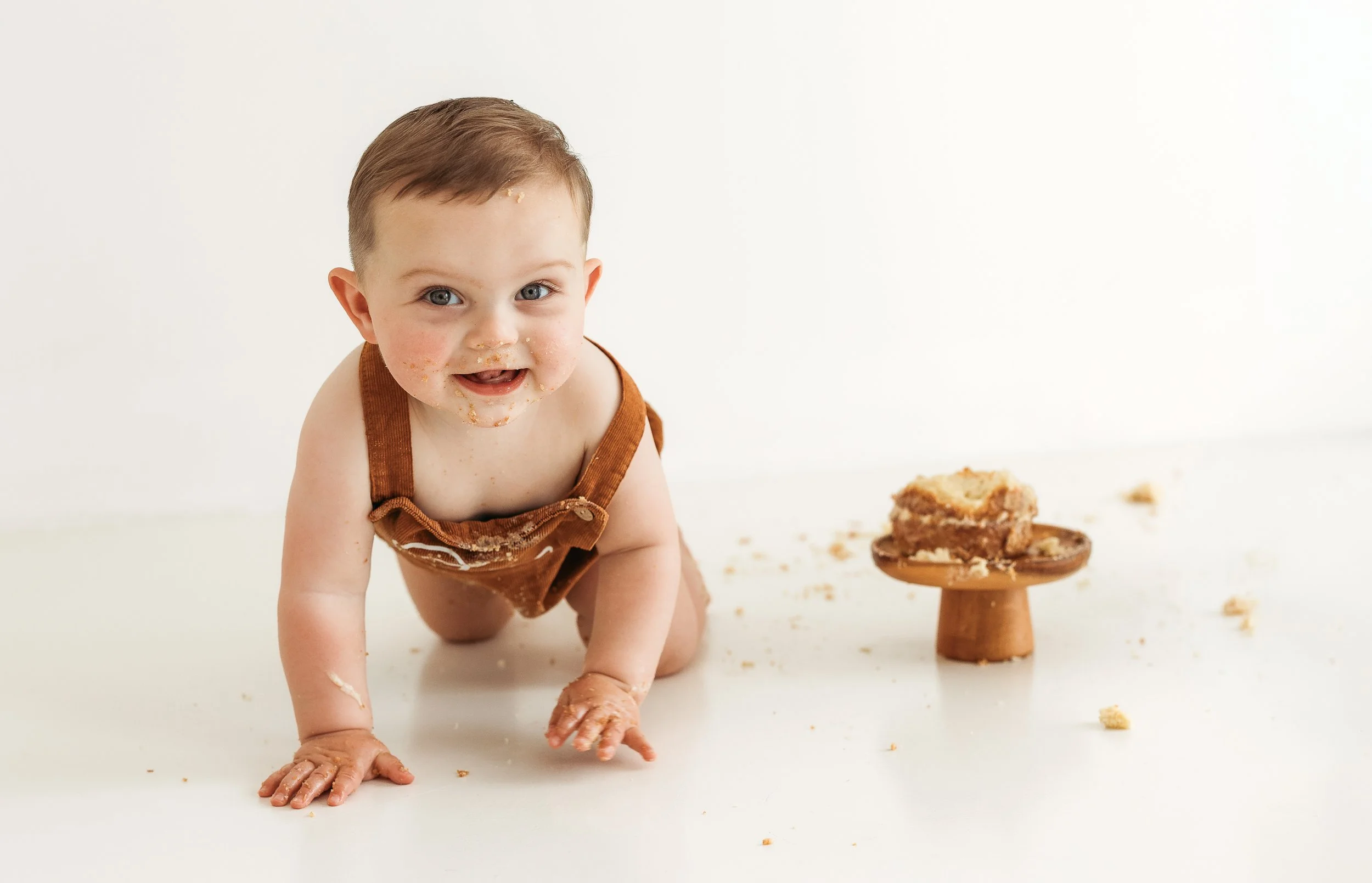 Happy toddler with cake-covered hands and face during a relaxed first birthday cake smash session.