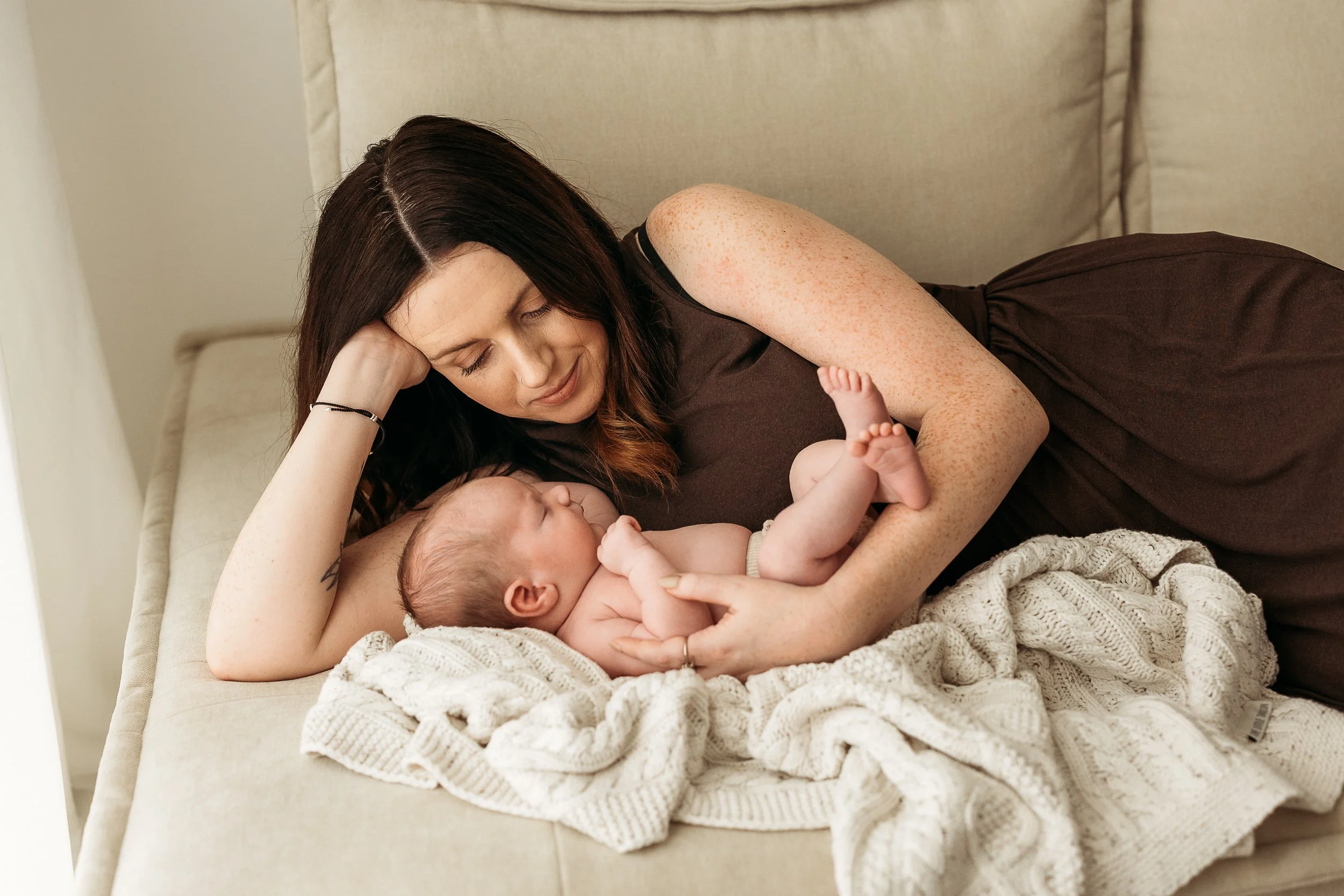 Mother cuddling her sleeping newborn baby during a relaxed newborn photography session.