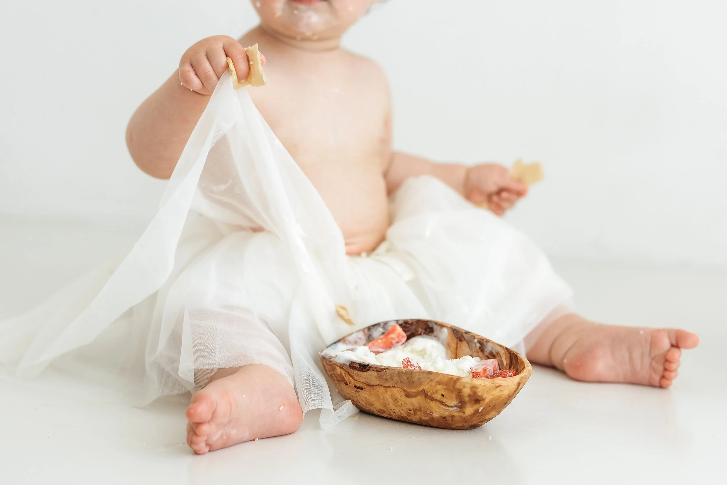 Baby exploring food with strawberries and cream during a first birthday photography session in a natural light studio