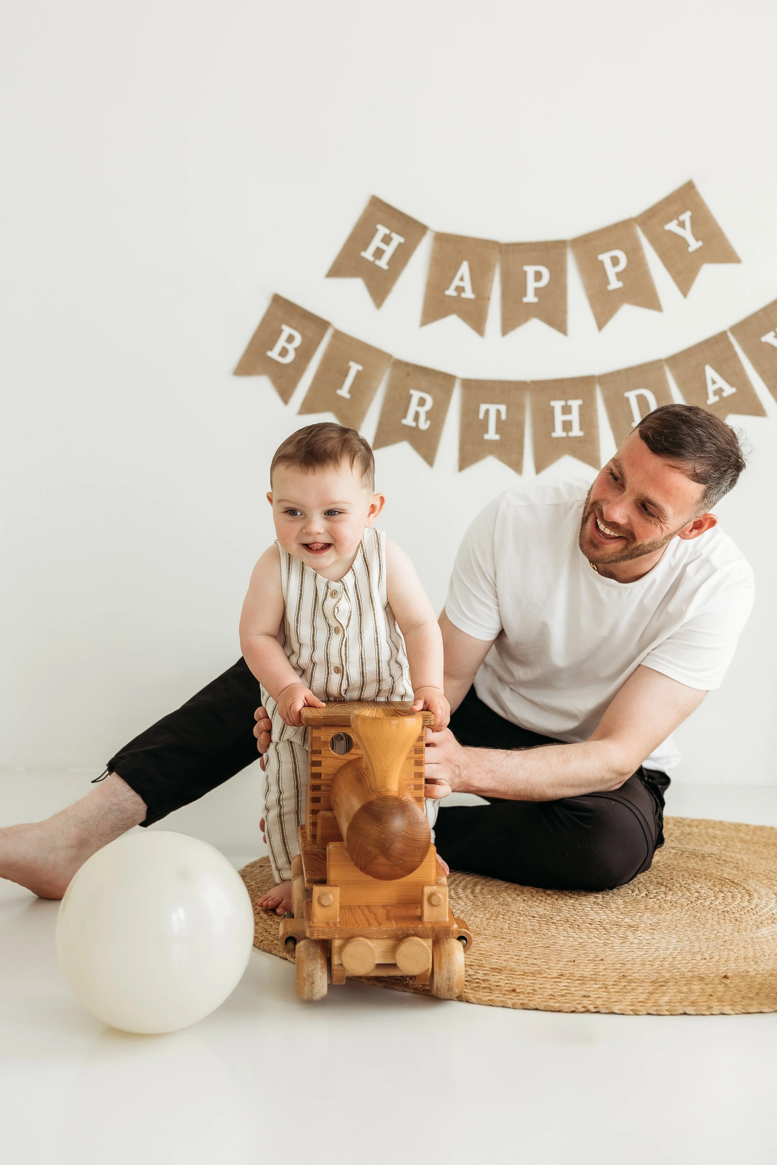 Father playing with his young daughter on a woven rug during a relaxed first birthday photography session at home.