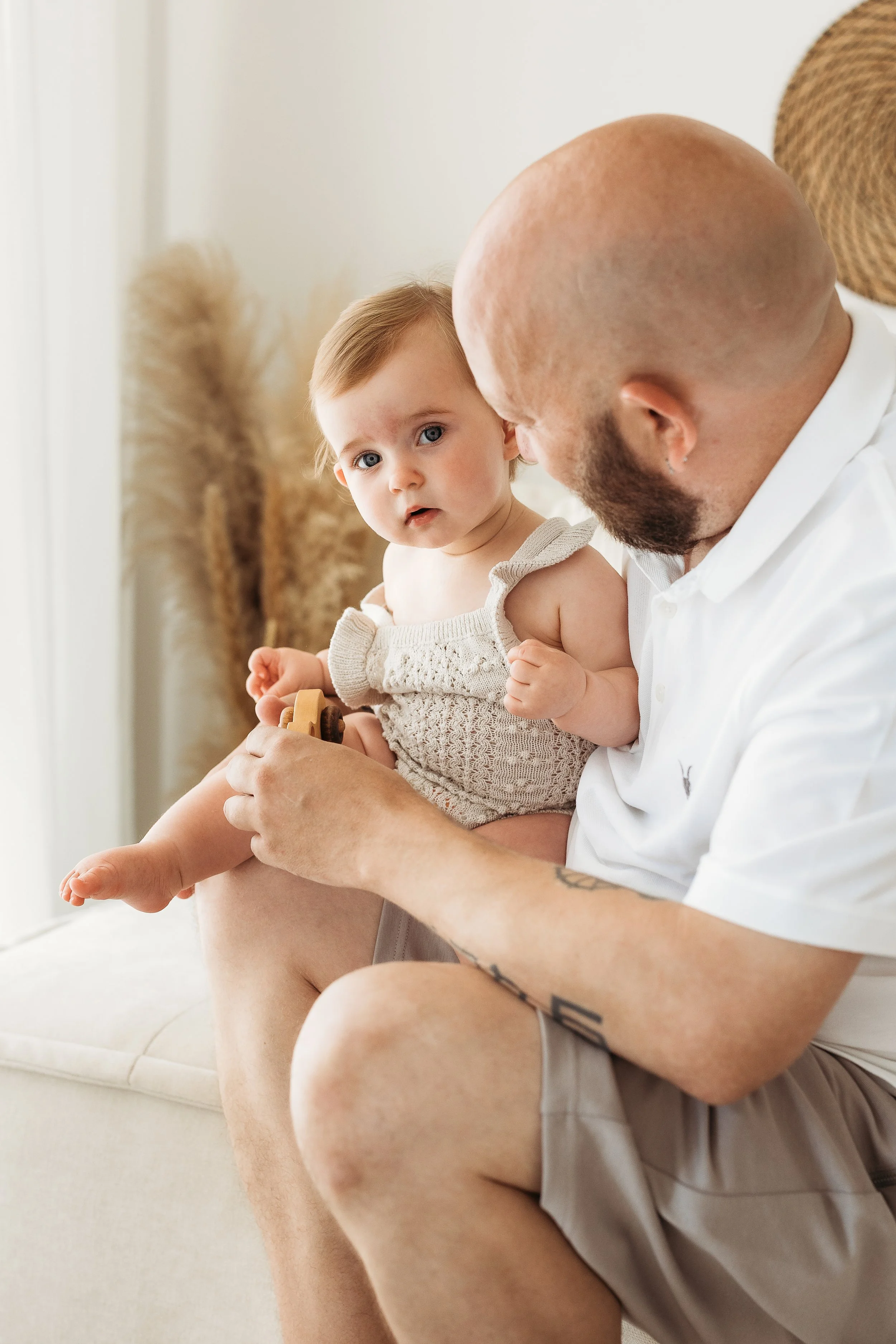 Father cuddling his young daughter on a white sofa during a relaxed first birthday photography session.