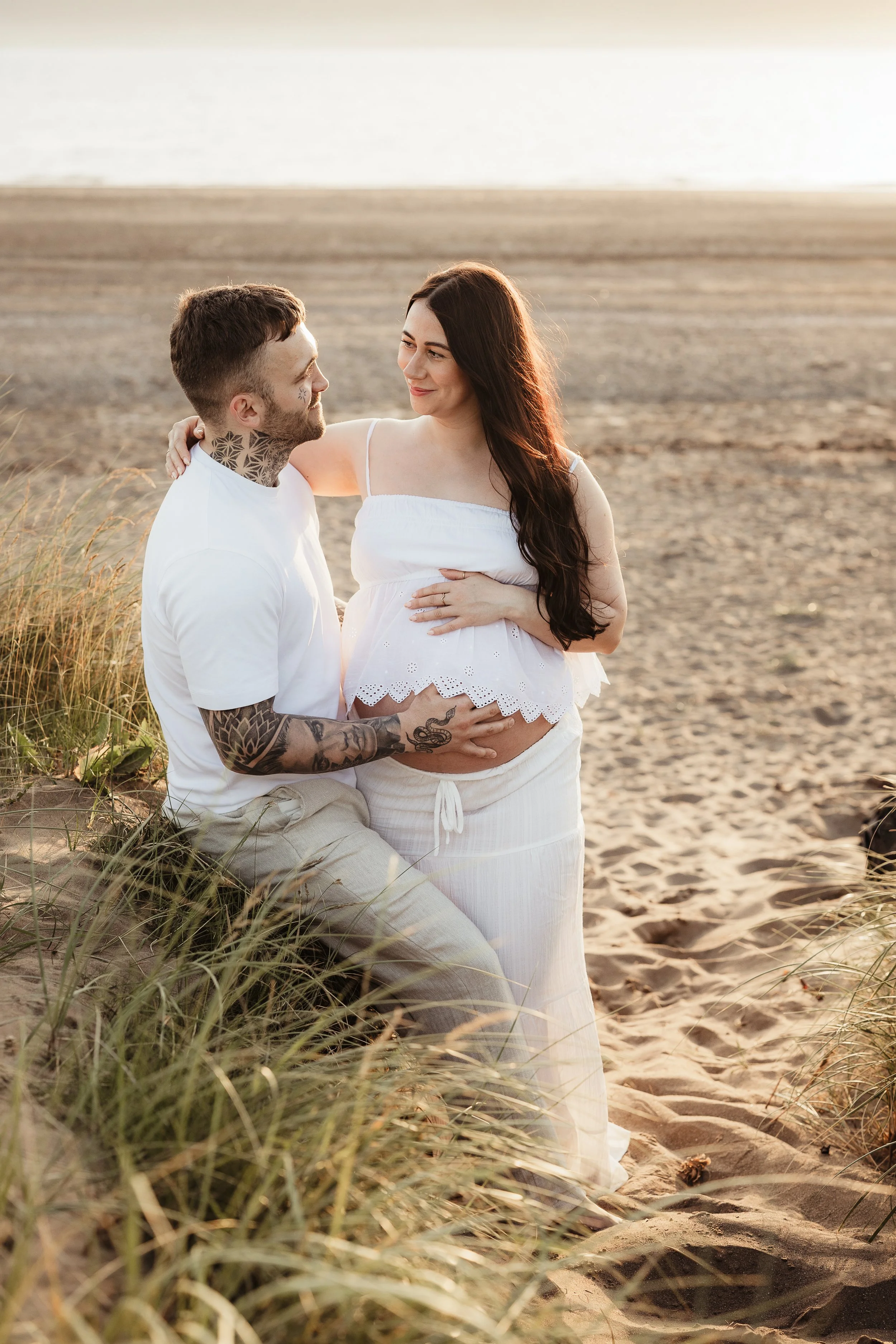 Expectant couple smiling together on the beach at sunset during an outdoor maternity session.