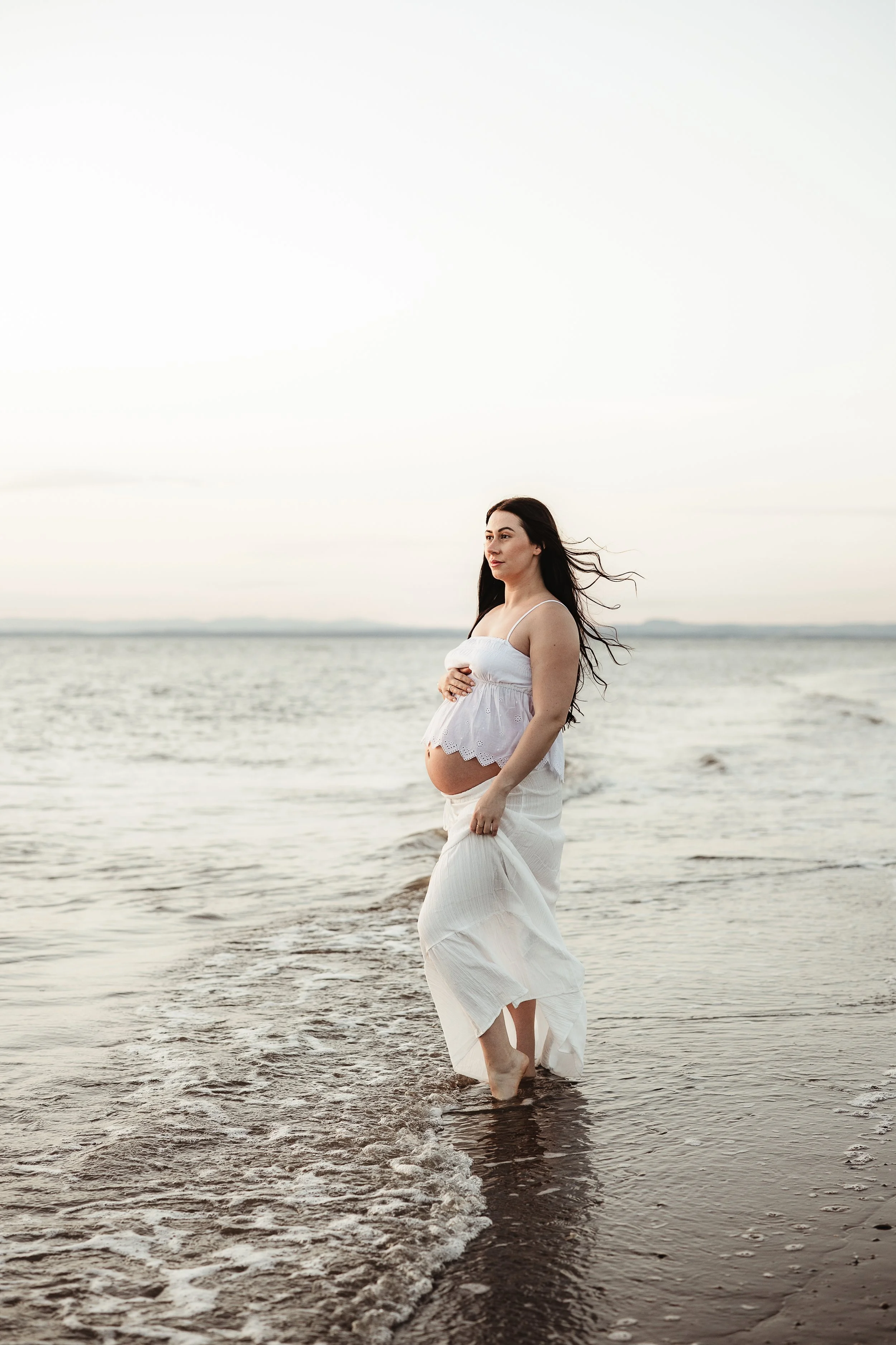 Pregnant woman standing barefoot in the sea at Silloth West Beach during a maternity photography session.