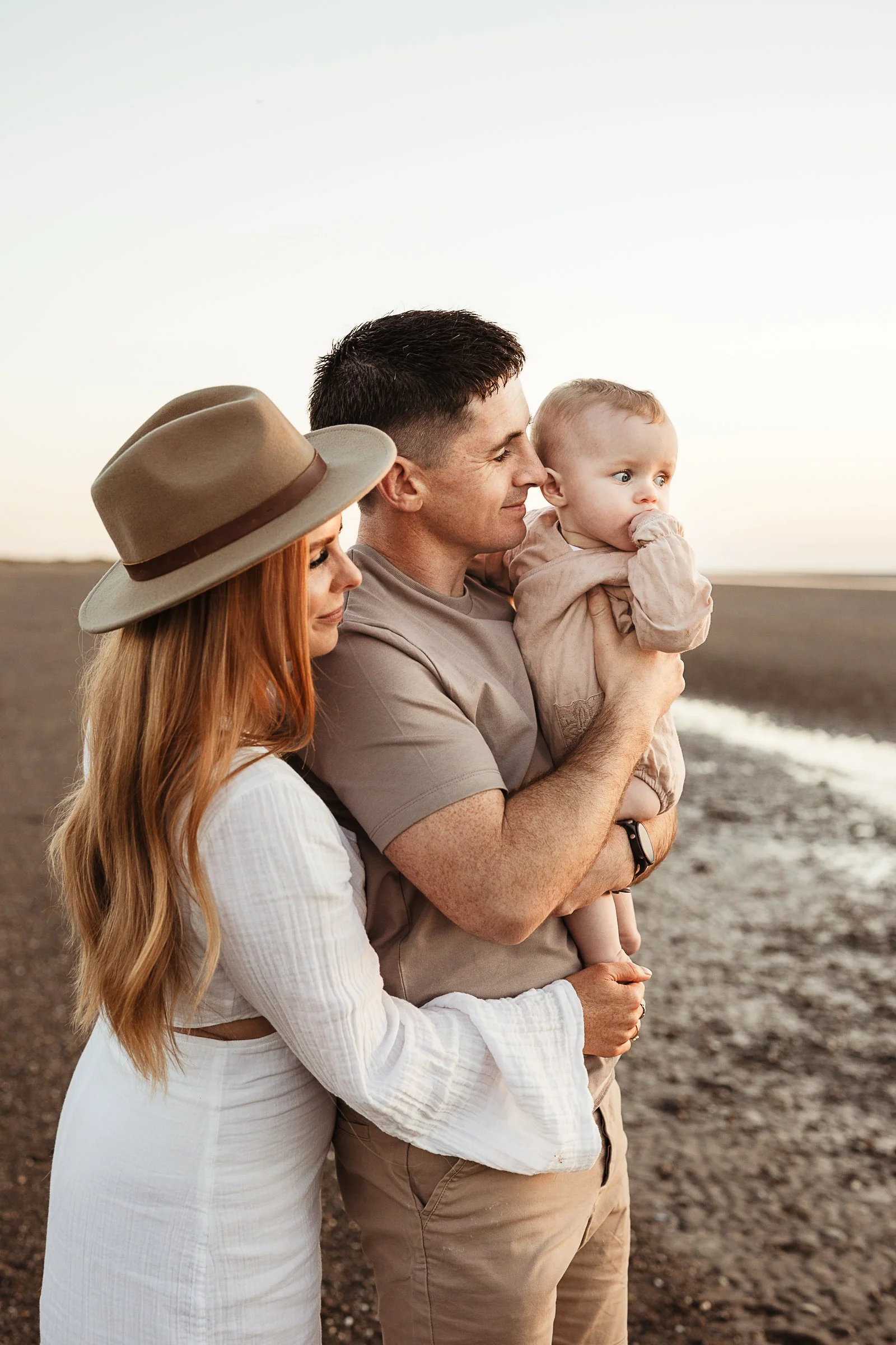 Parents cuddling their young daughter on the beach during a relaxed family photography session.