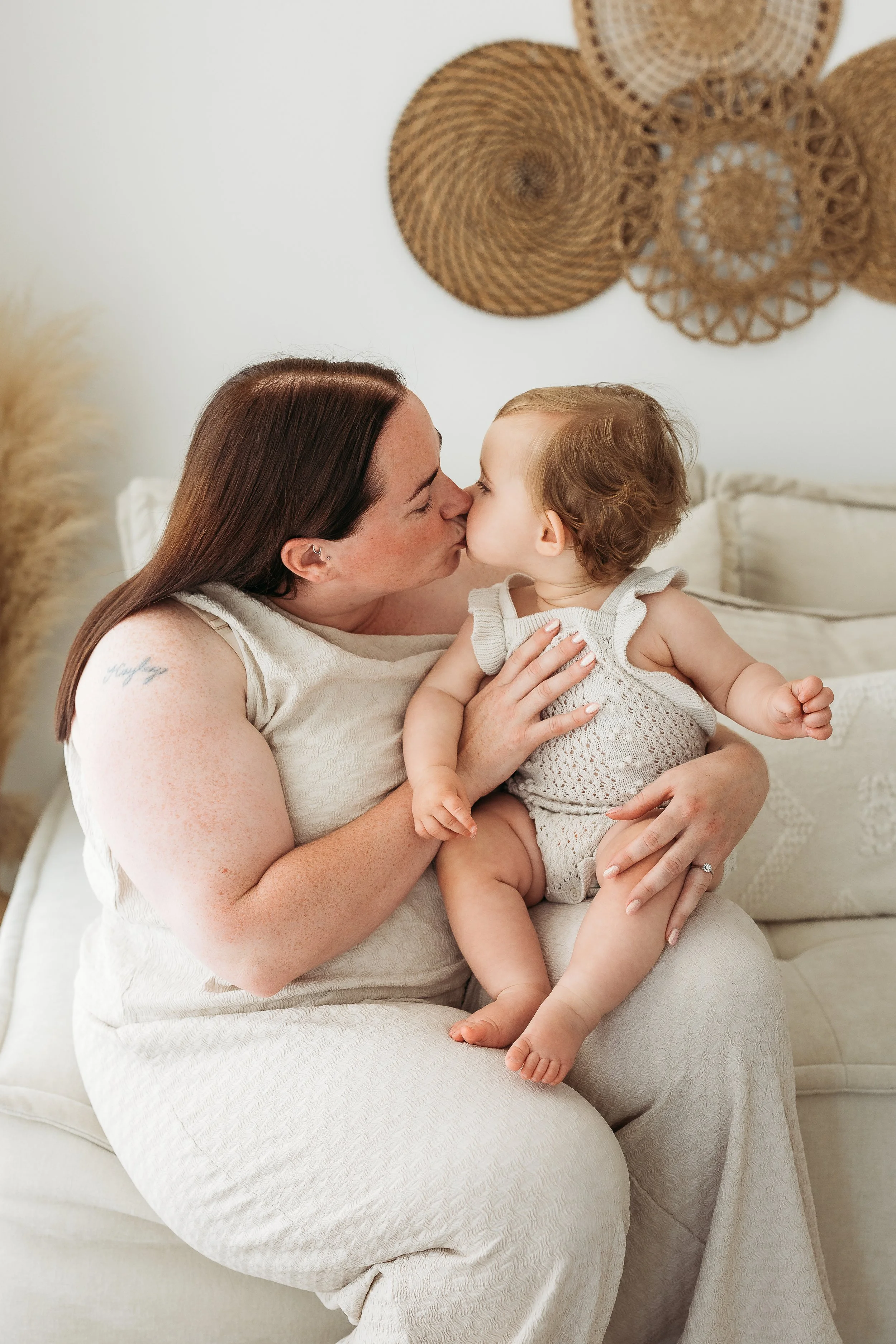 Mother cuddling and kissing her child during a relaxed first birthday photography session in a natural light studio.