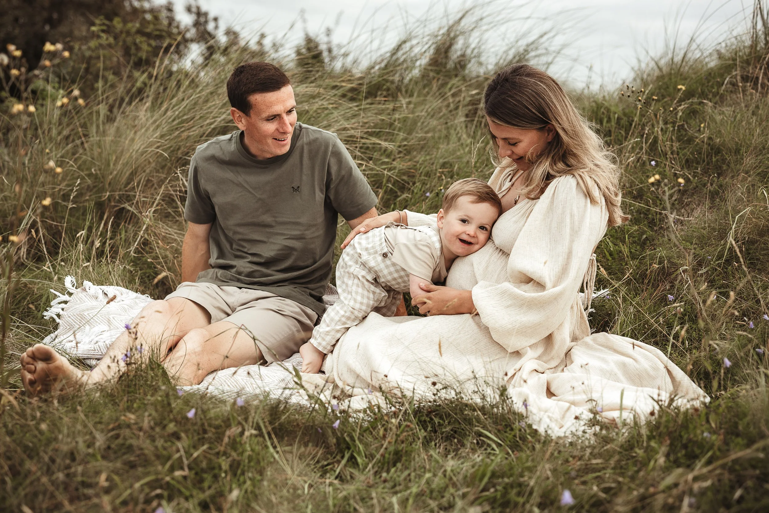 Expecting parents sharing a quiet moment outdoors with their young child during a relaxed maternity photography session.