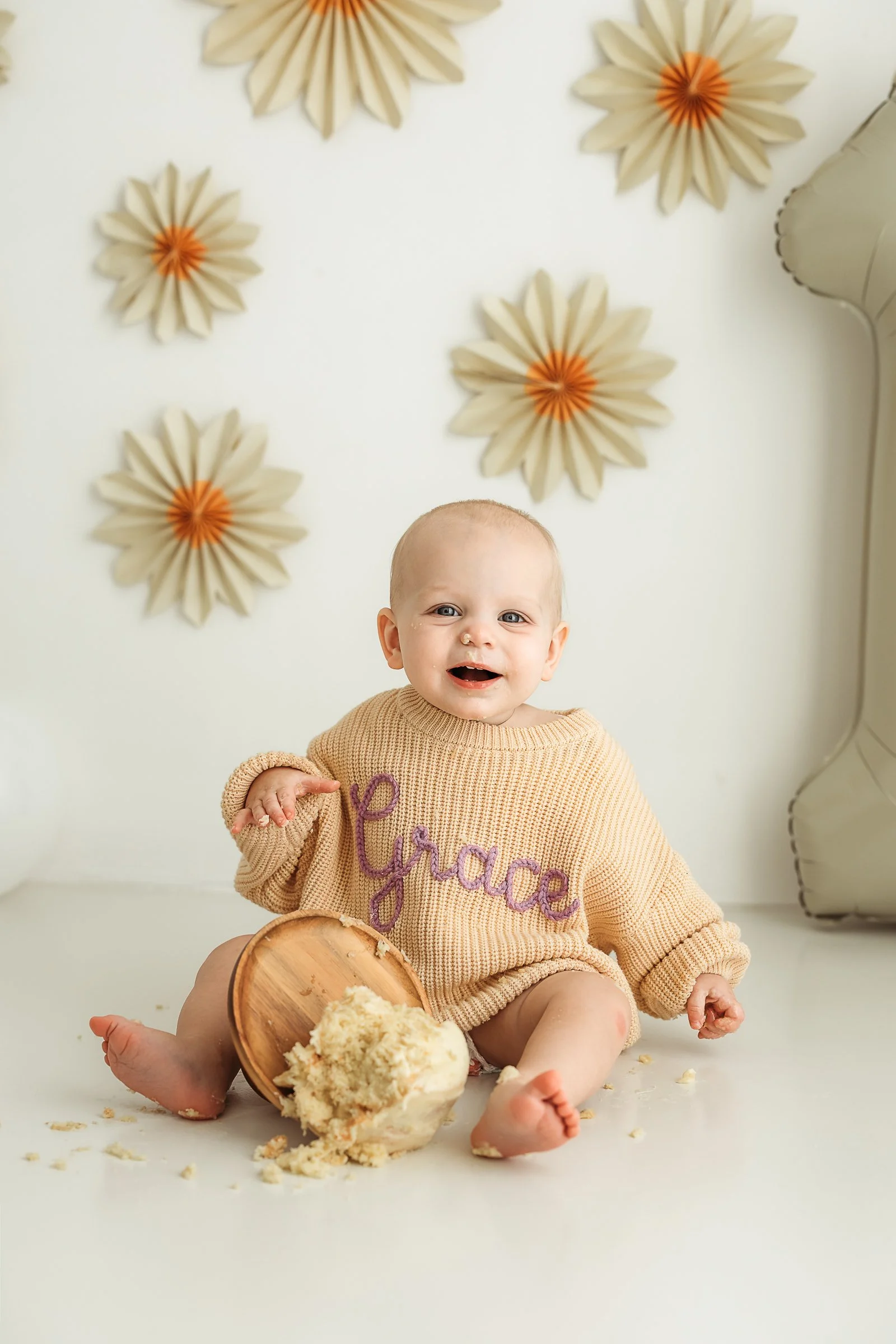 Smiling baby enjoying a simple first birthday cake smash in a natural-light studio.