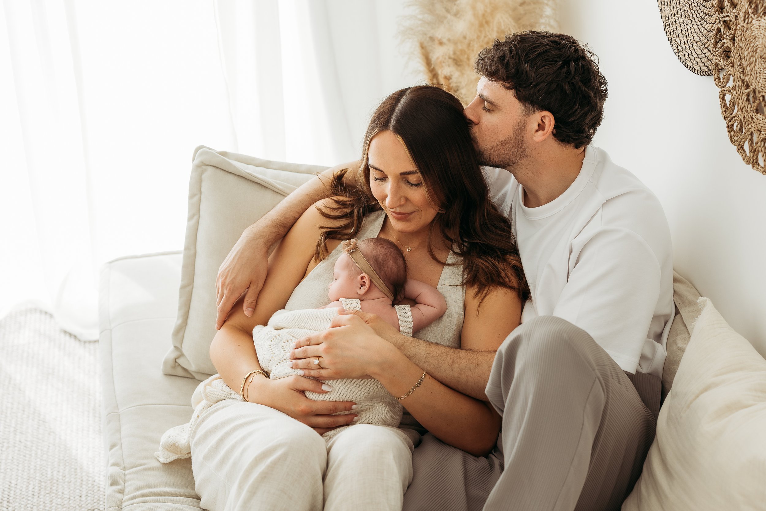 Parents cuddling and kissing their newborn baby during a natural family newborn photography session.