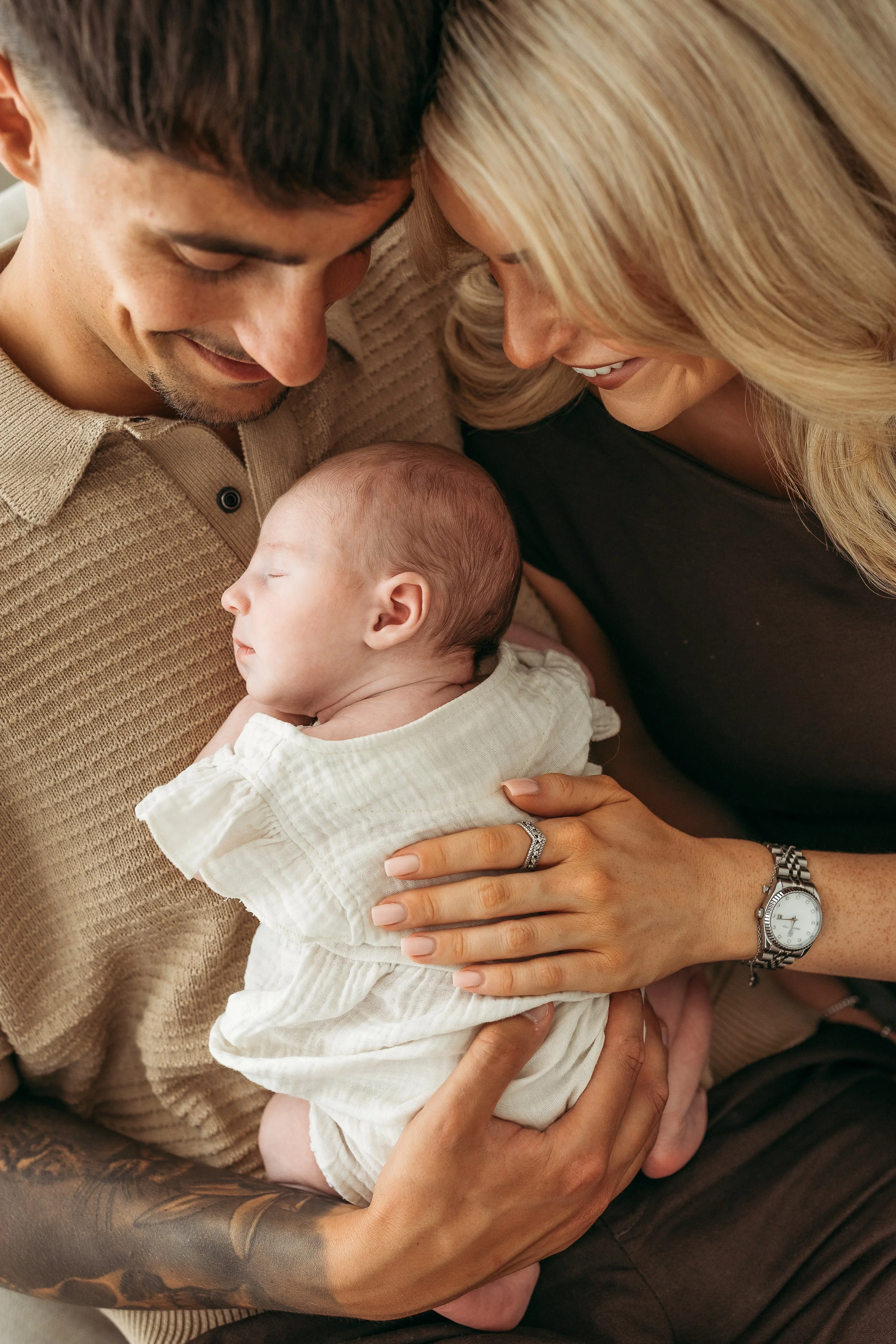 Parents cuddling their sleeping newborn baby during a relaxed newborn session.