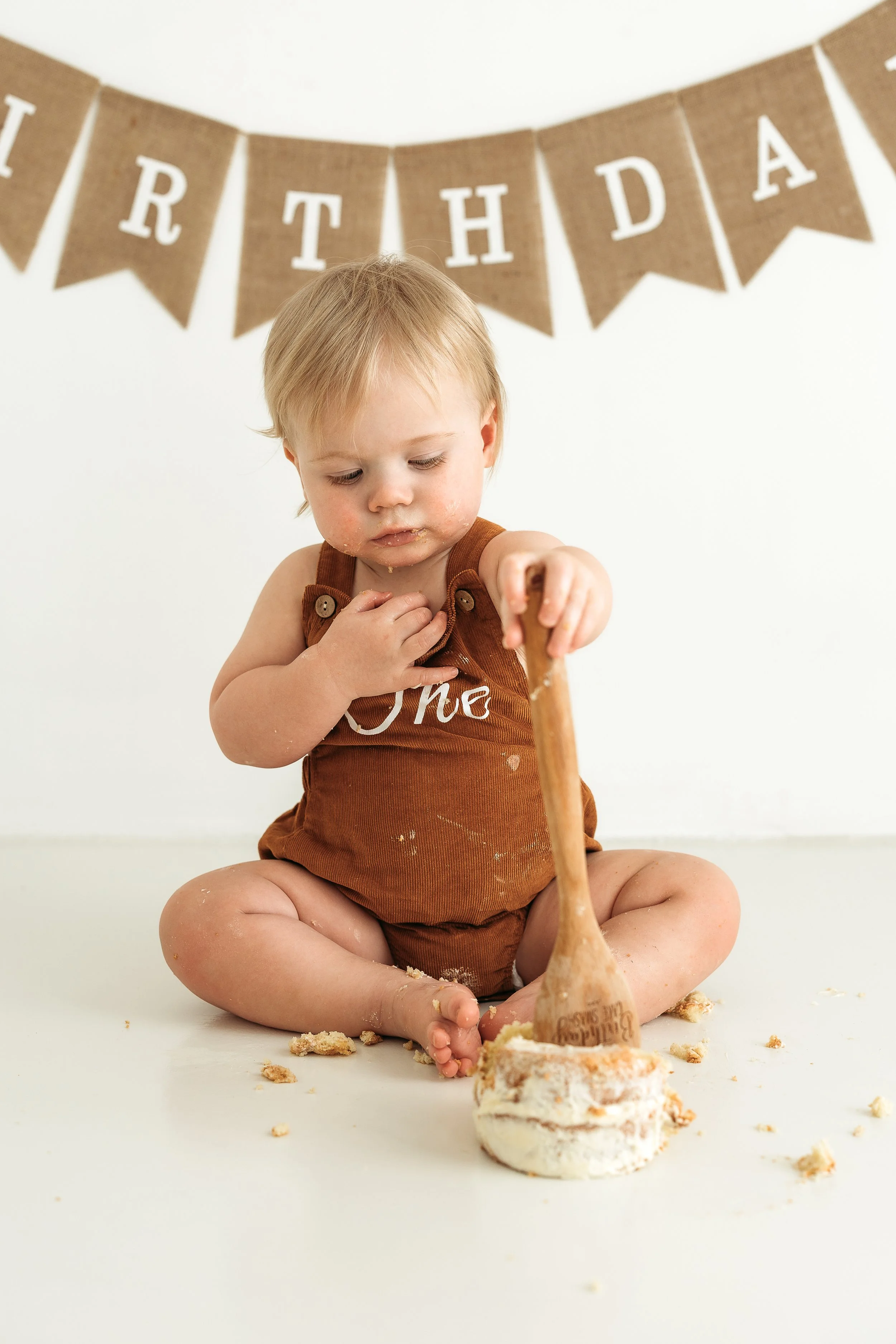 One year old child enjoying cake with messy hands and crumbs during a first birthday photography session