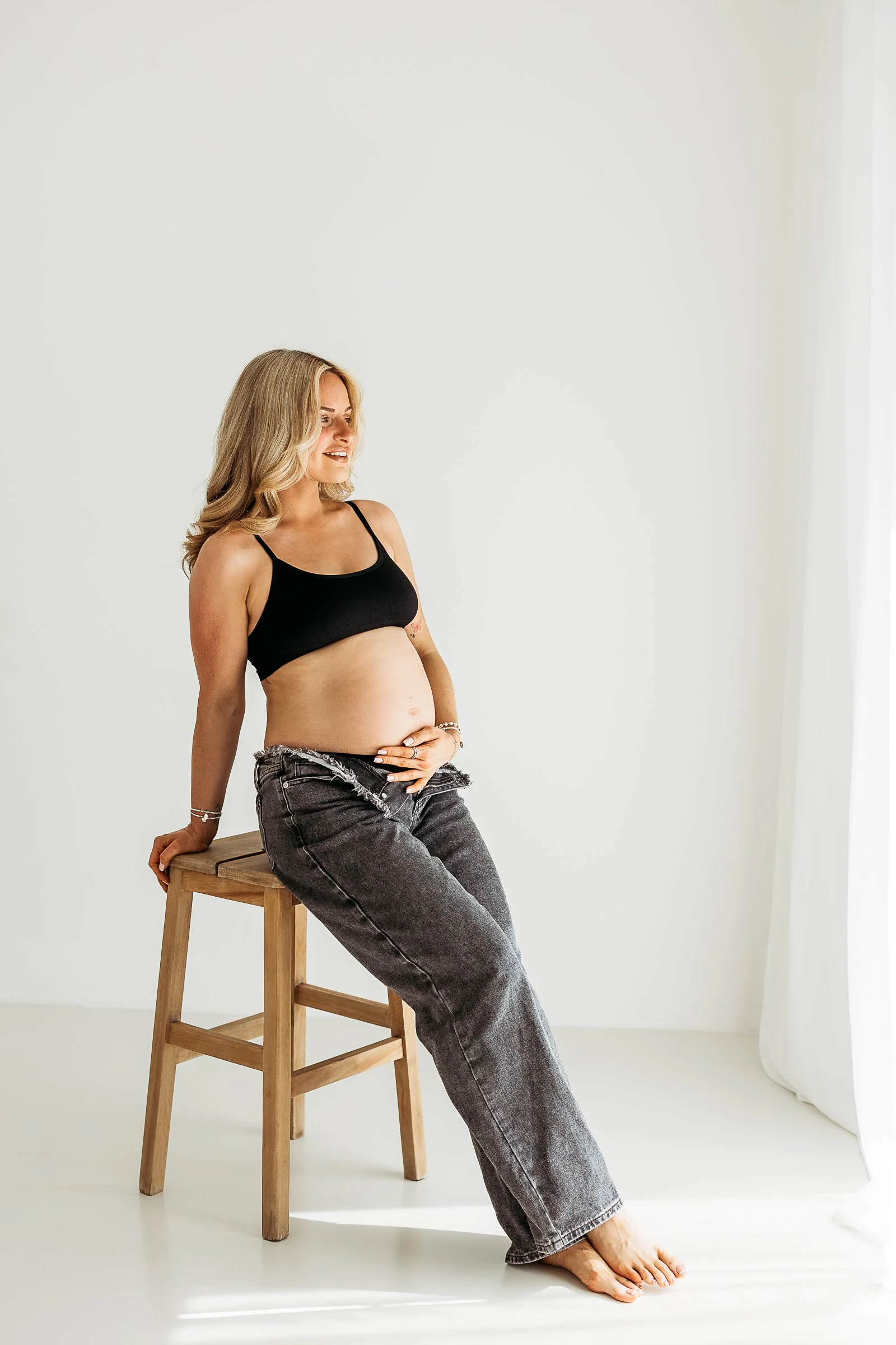 Pregnant woman seated in a bright, natural-light photography studio.