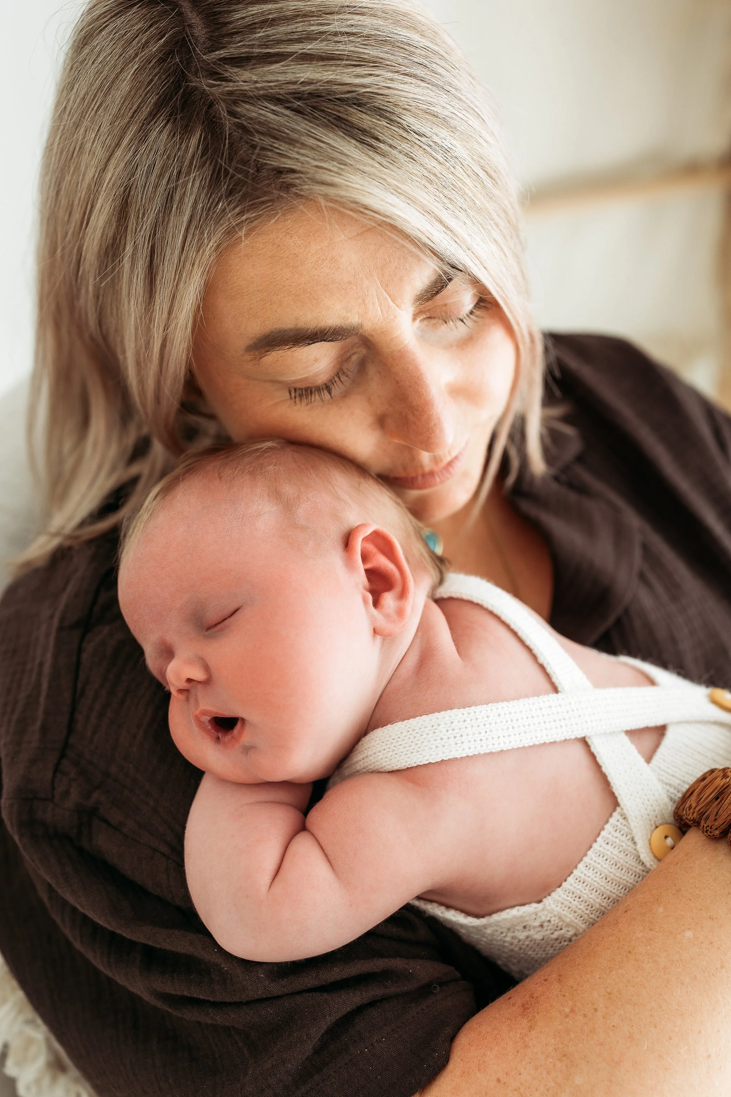 A woman with blonde hair and closed eyes holding a sleeping baby close to her face.