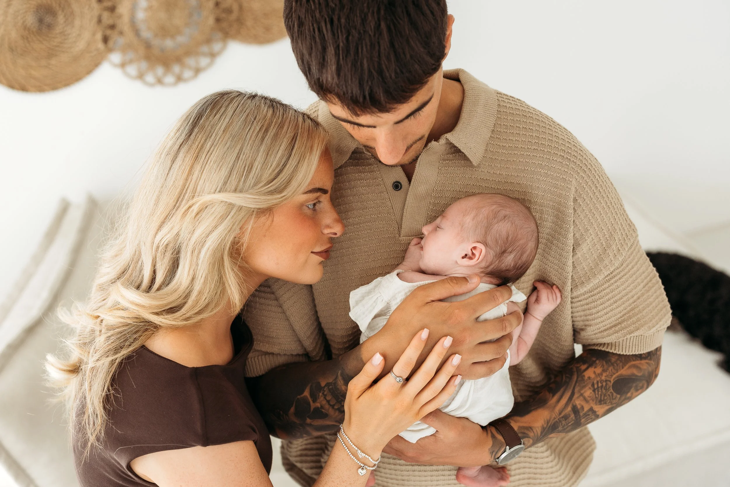 Parents lovingly holding their newborn baby together during a natural lifestyle newborn photography session.