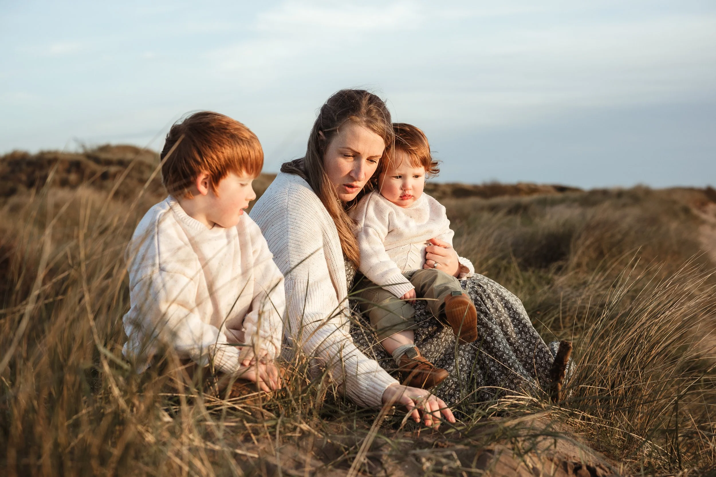 A mother and her children sharing a quiet moment together in the grass, capturing the closeness and connection of everyday family life.