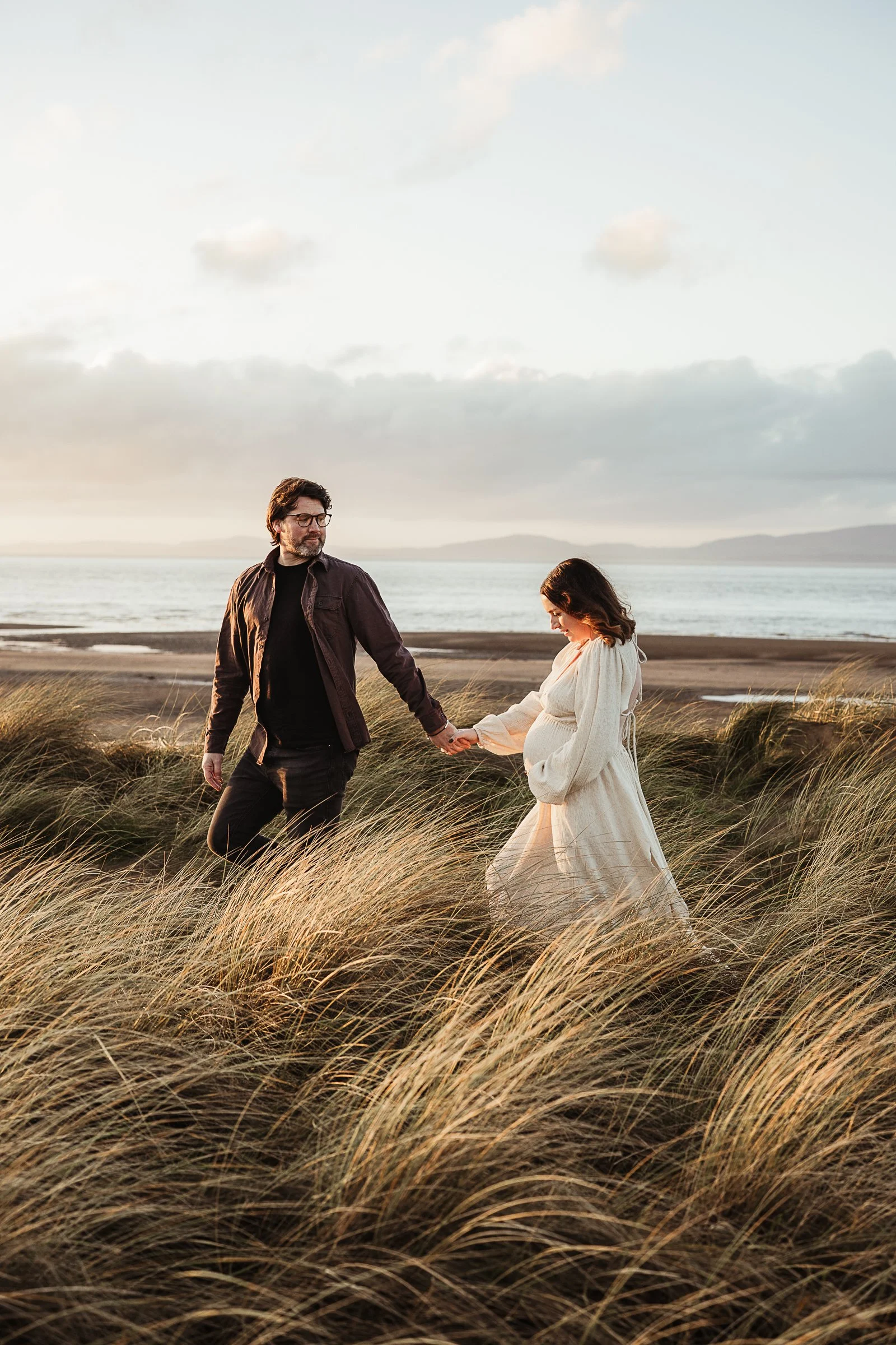 Expecting parents walking hand in hand through the landscape during a relaxed outdoor maternity photography session.