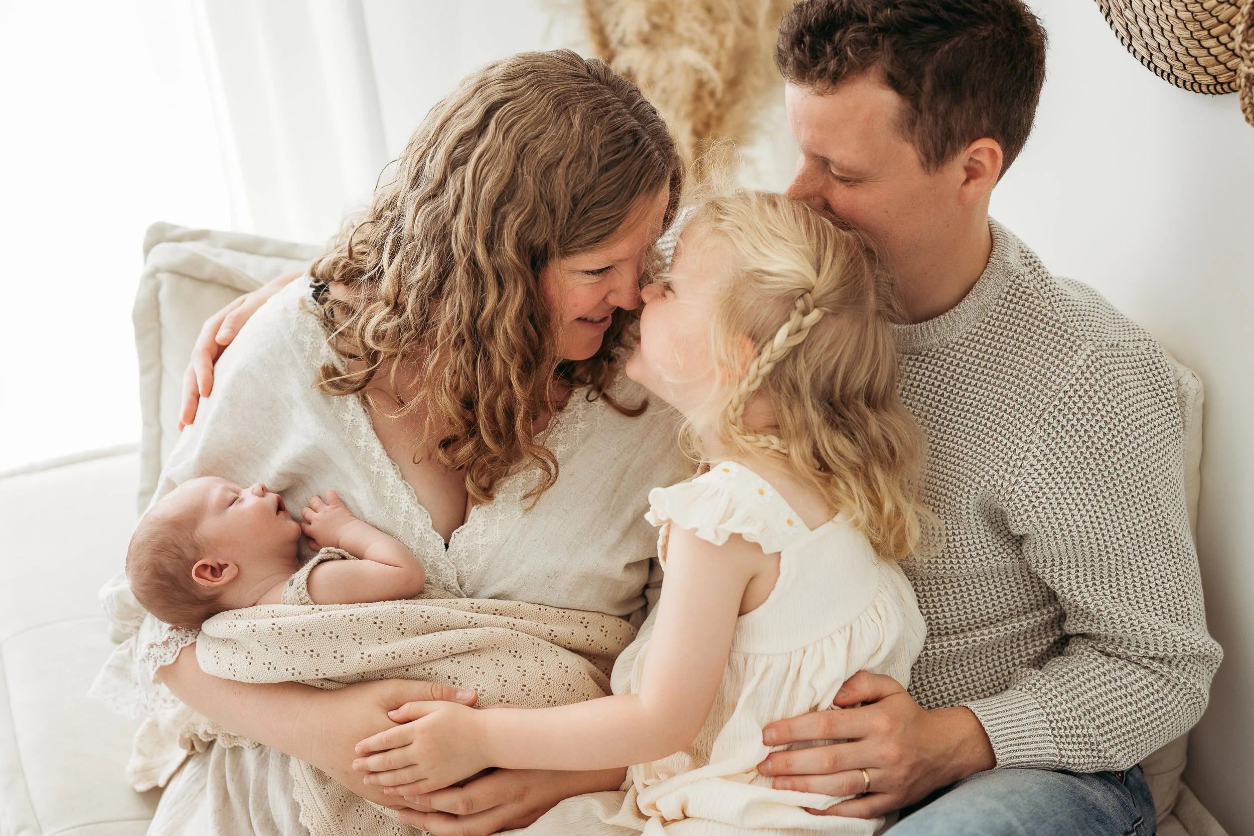 Family of four sharing a loving moment during a relaxed newborn photography session.