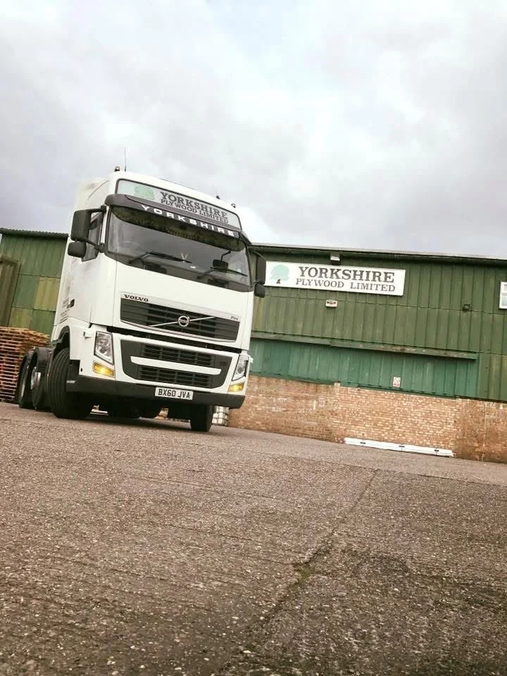 White Volvo truck parked outside of a green industrial building with a sign that reads 'Yorkshire Plywood Limited'.