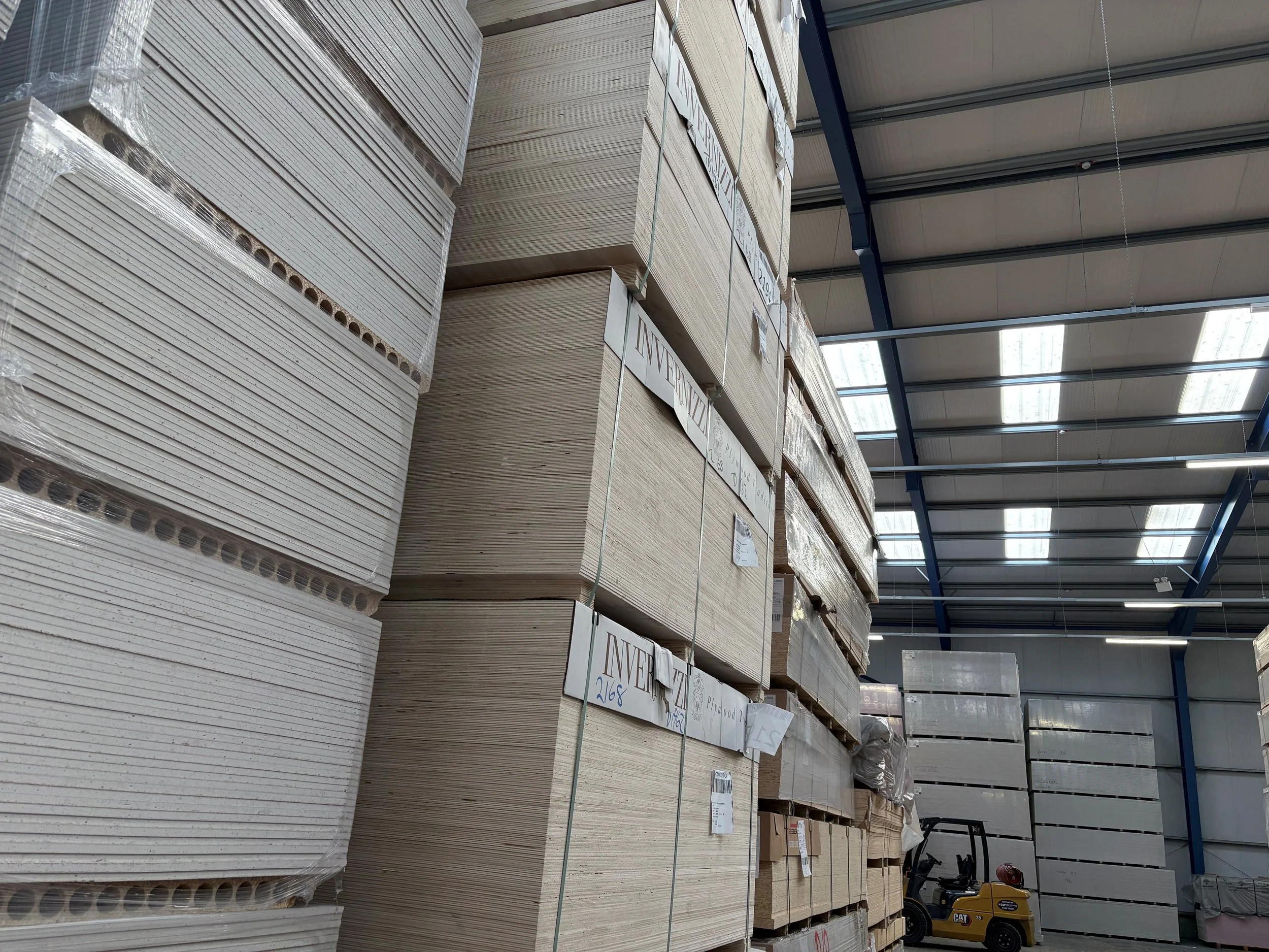 Stacks of panels stored vertically in a warehouse with a forklift in the background.