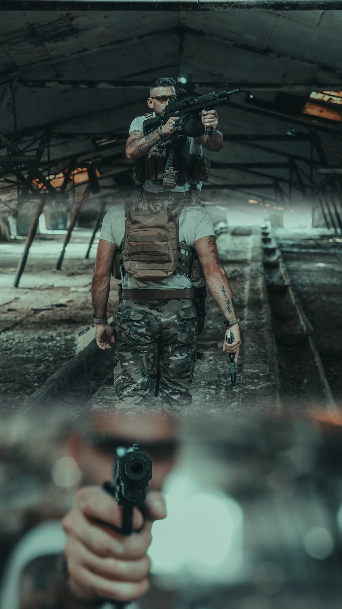 A person in military camouflage holding a gun and pointing it at the camera, with another person aiming a gun from behind in an abandoned building.