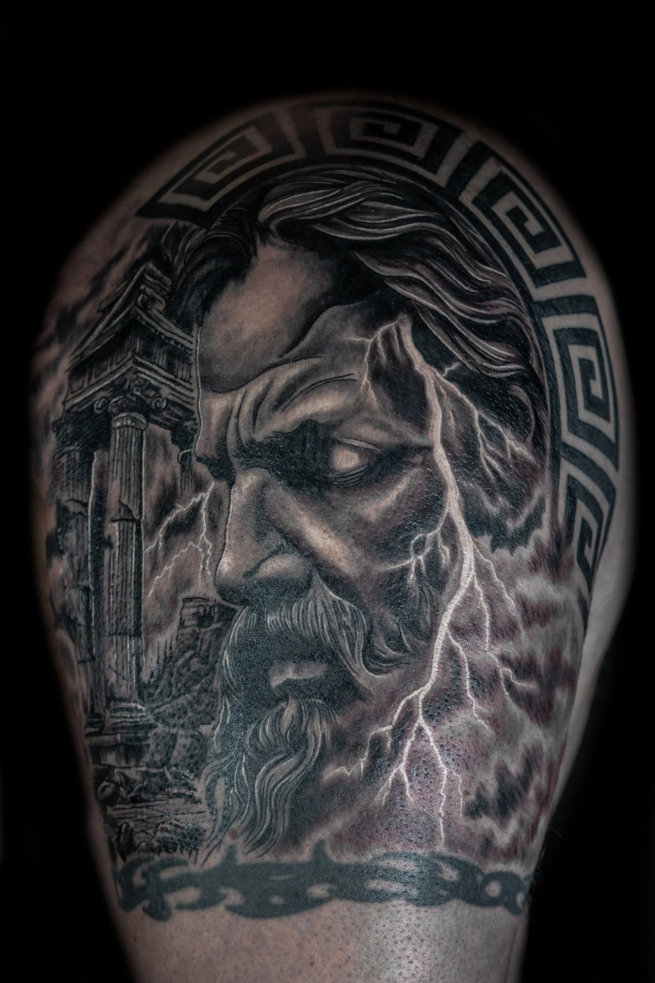 Tattoo of a woman's face with flowing hair, lightning, and Greek key border design.
