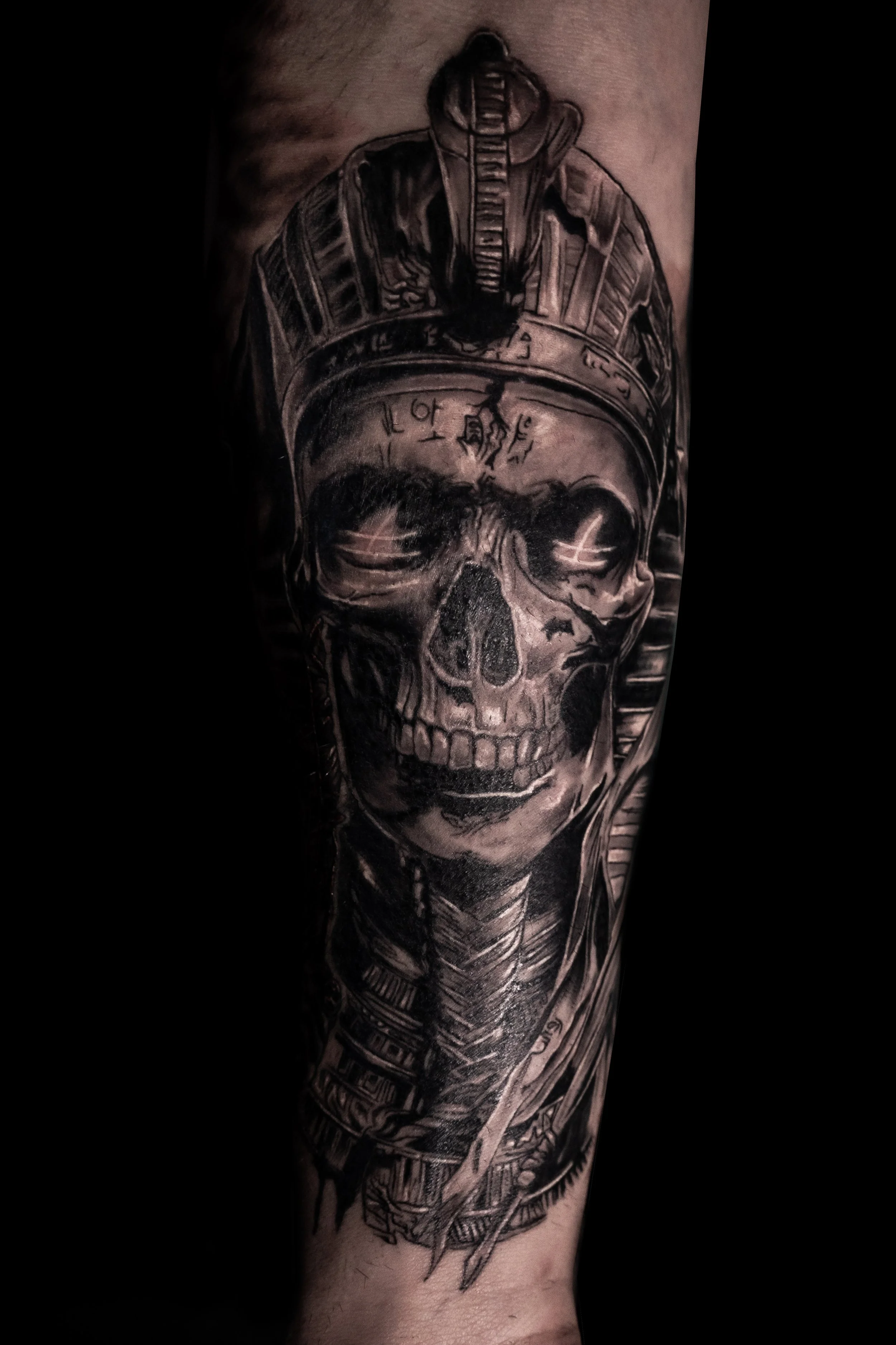 A black and gray tattoo of a human skull wearing a military helmet, with various detailed elements including a sword and other decorative patterns.