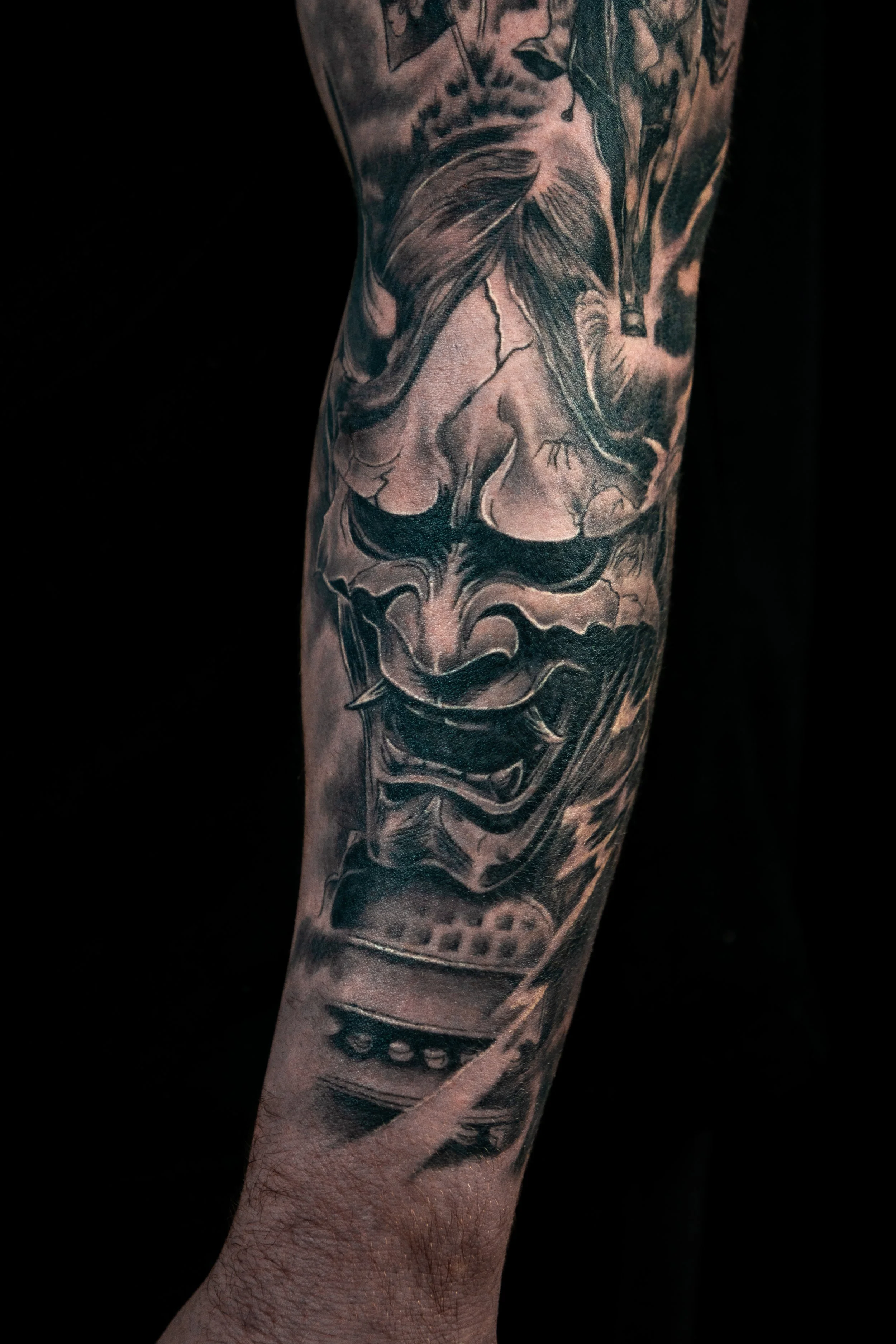 Black and gray tattoo sleeve featuring a depiction of a person with long hair in a realistic style on the upper arm. The design includes intricate shading and detail, with other abstract elements.