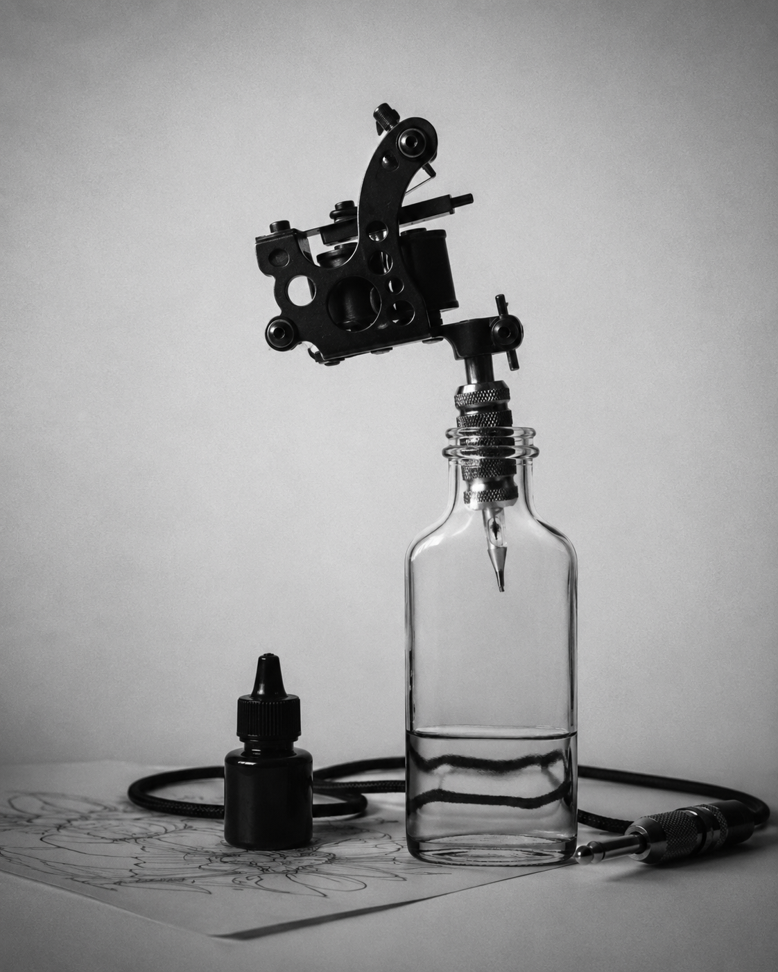 Machine à tatouer montée sur une bouteille en verre, accompagnée d’encre et d’une alimentation.
