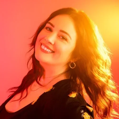 A woman with long dark hair smiling against a colorful, orange-pink gradient background