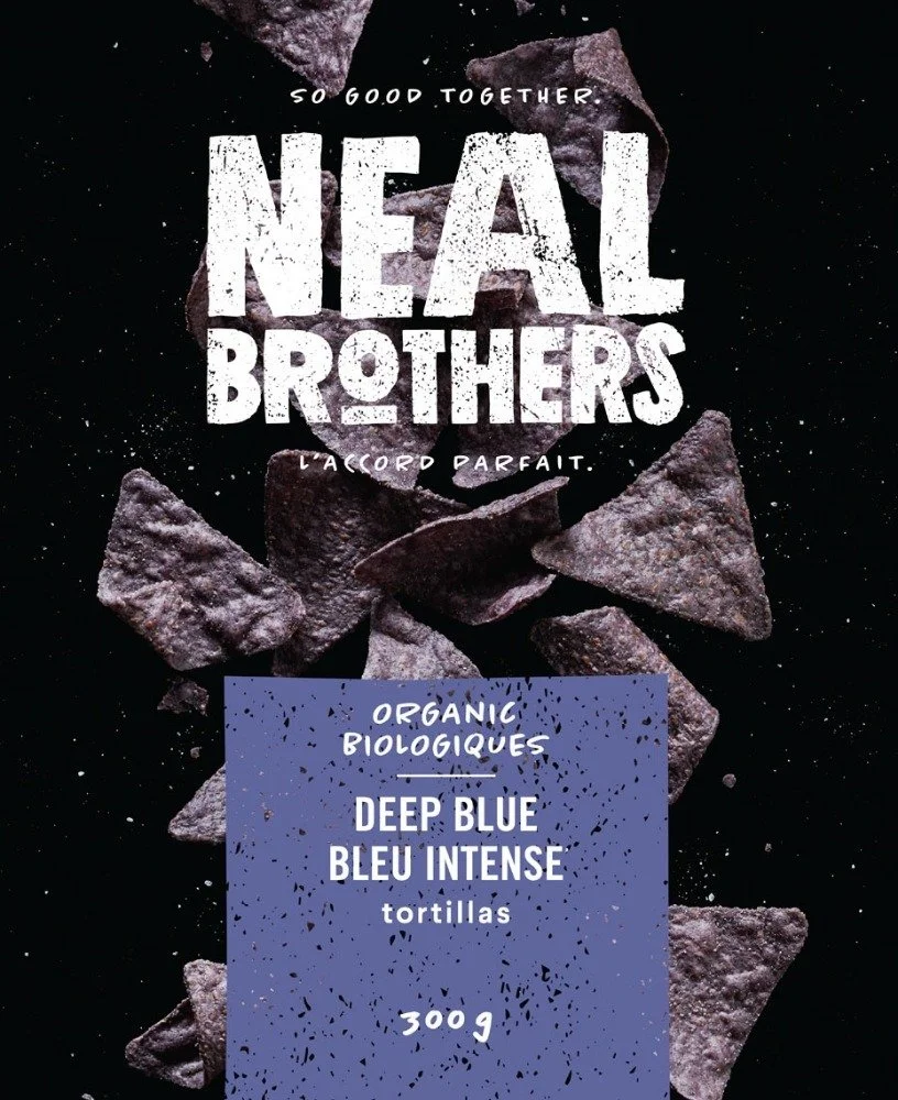 Package of organic blue corn tortilla chips with a dark background and scattered chips visible.