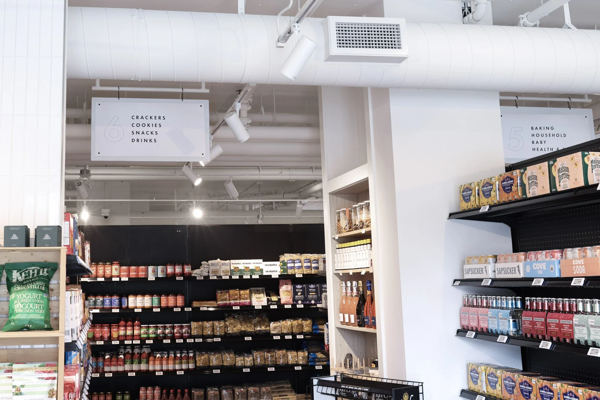 Aisle in a grocery store with shelves of food products and signs indicating snack and baking sections.